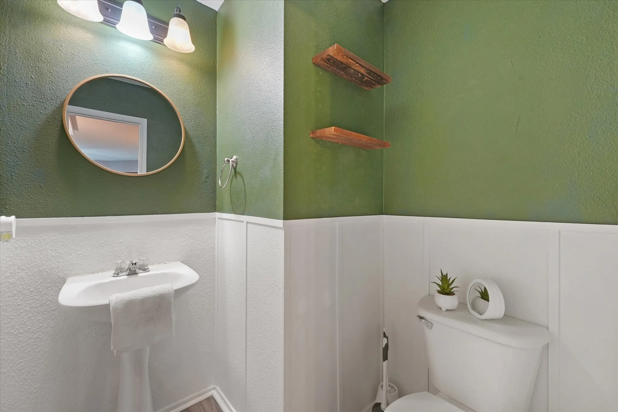 Pedestal sink with chrome faucet, complemented by a round framed mirror and three-light vanity fixture