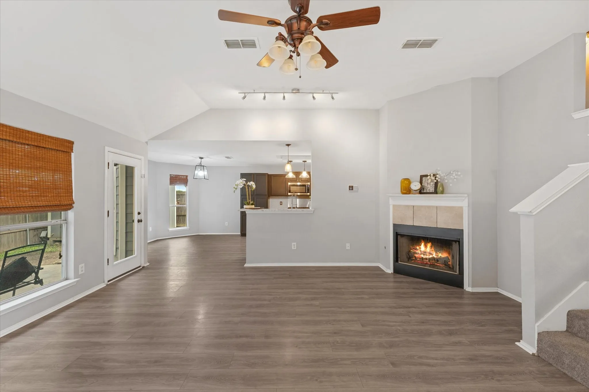 Spacious living area featuring wood-finish flooring, vaulted ceilings, and a corner fireplace with a tiled surround