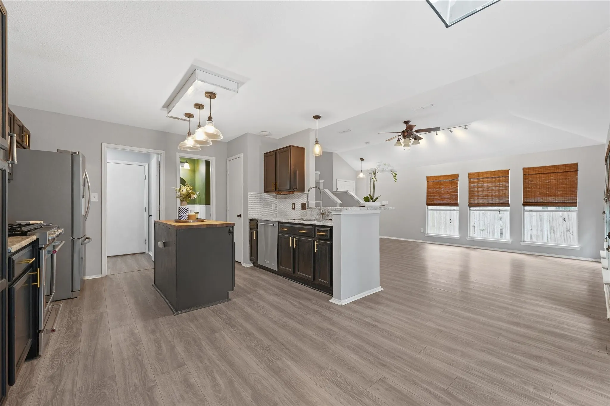 Open-concept kitchen featuring an island with a butcher block countertop, dark wood-finish cabinetry, stainless steel appliances, and wood-finish flooring extending into the living area