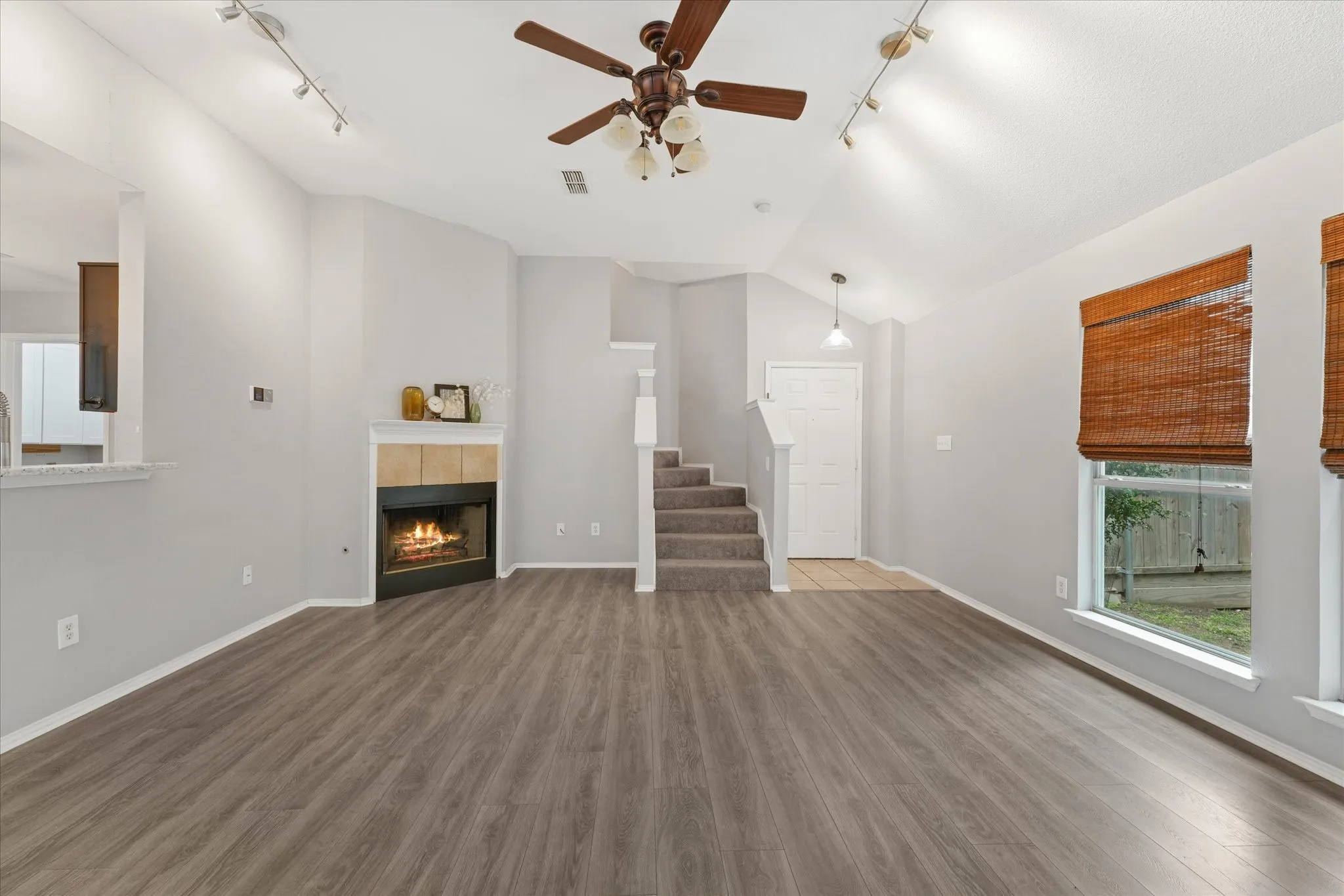 Spacious living area featuring wood-finish flooring, a corner fireplace with a tile surround and mantel, and vaulted ceilings