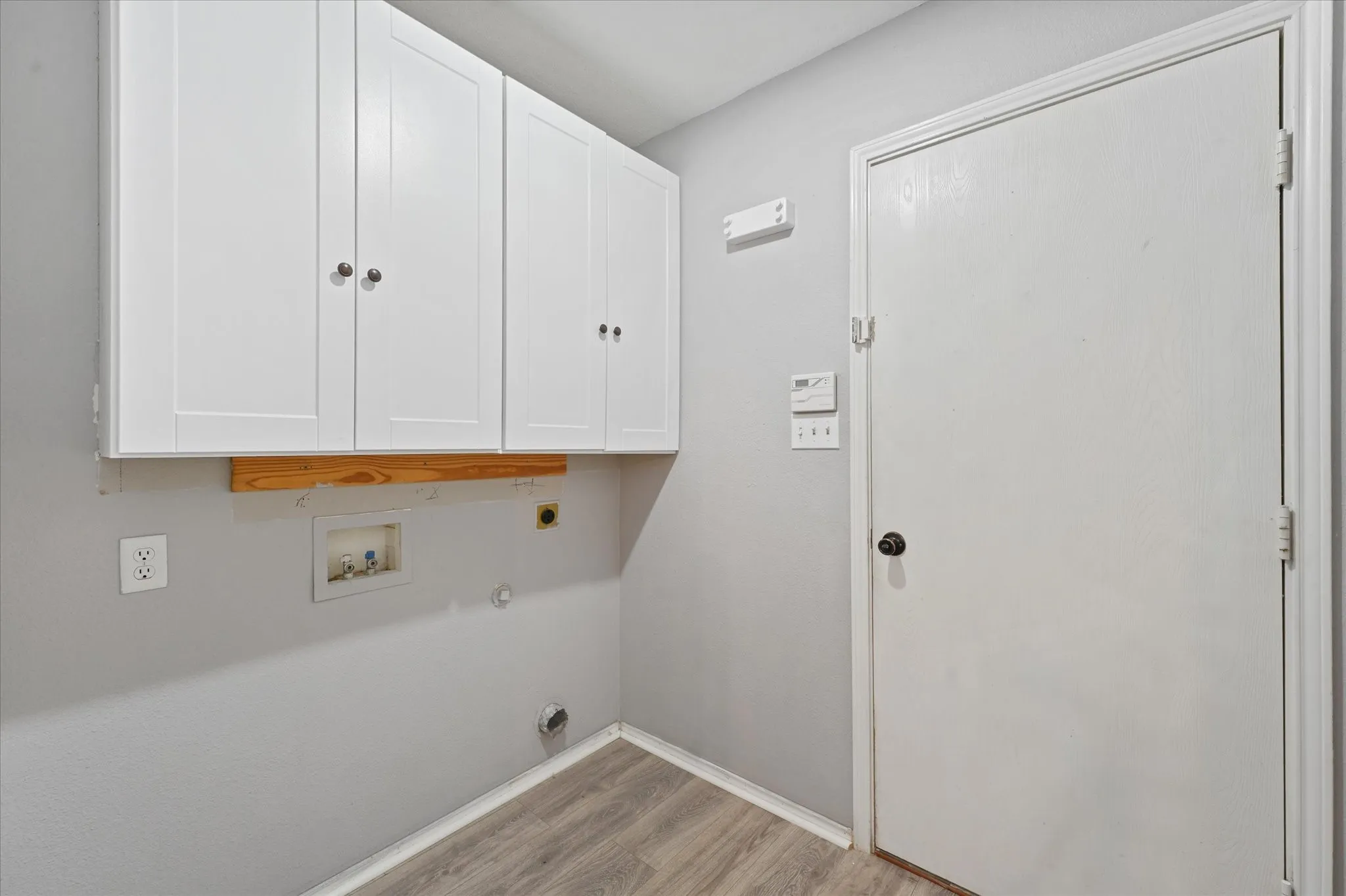 Utility space featuring white shaker-style cabinetry, wood-finish flooring, and light gray wall paint