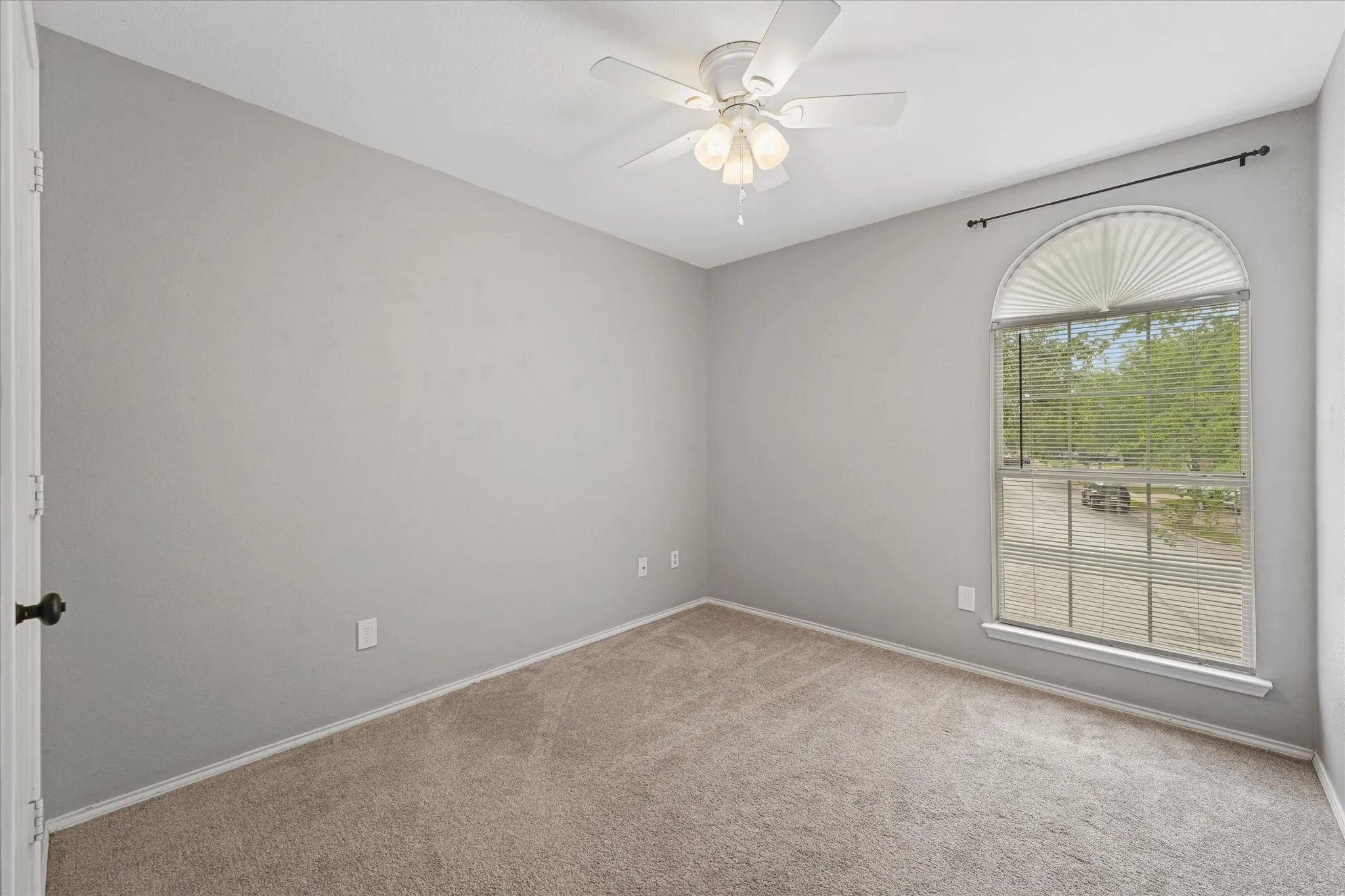 Neutral gray walls featuring an arched window with blinds, a ceiling fan with integrated lighting, and carpet flooring
