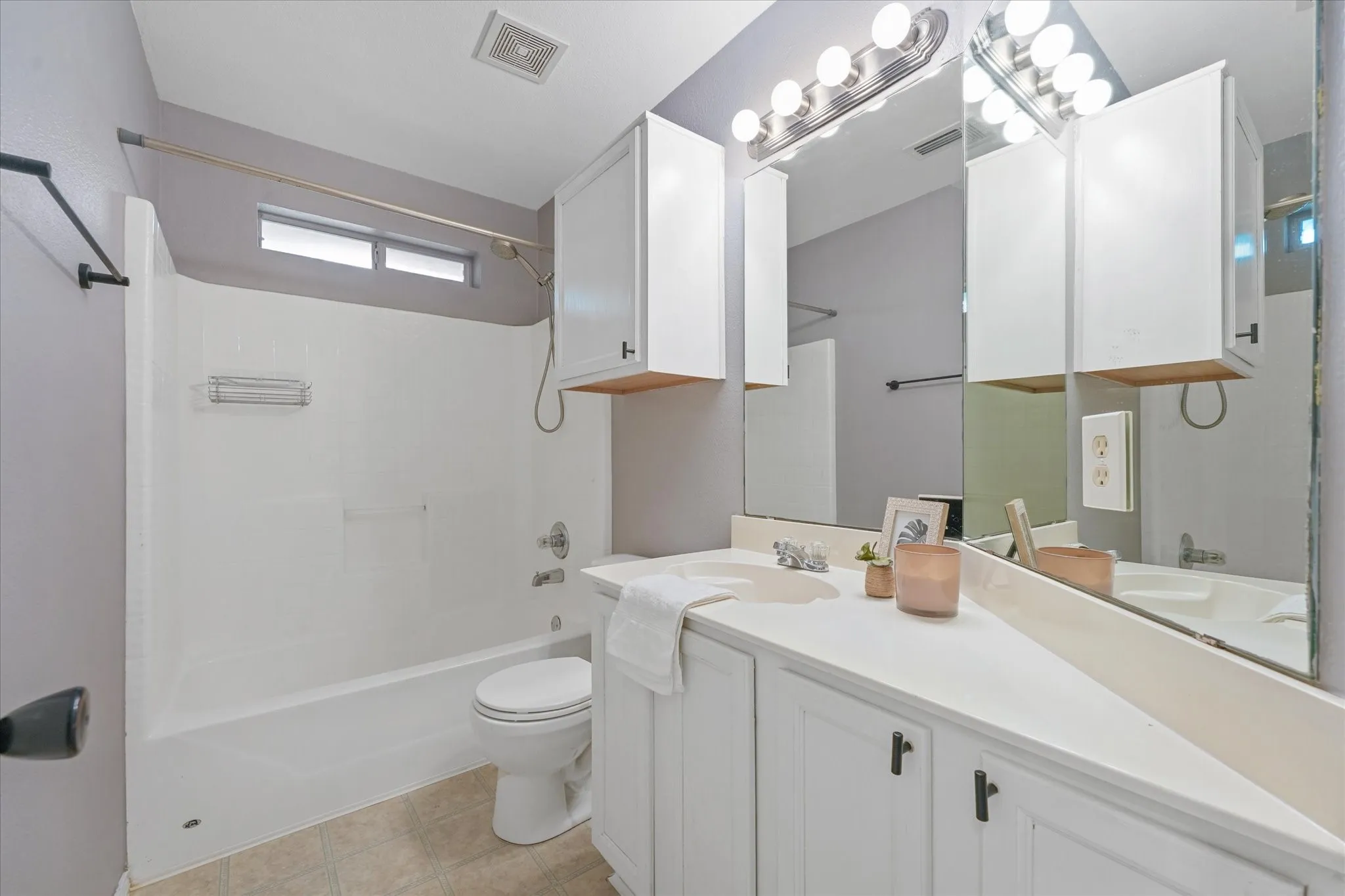 Bathroom featuring a white vanity with integrated sink, white cabinetry, and a large mirror with overhead lighting