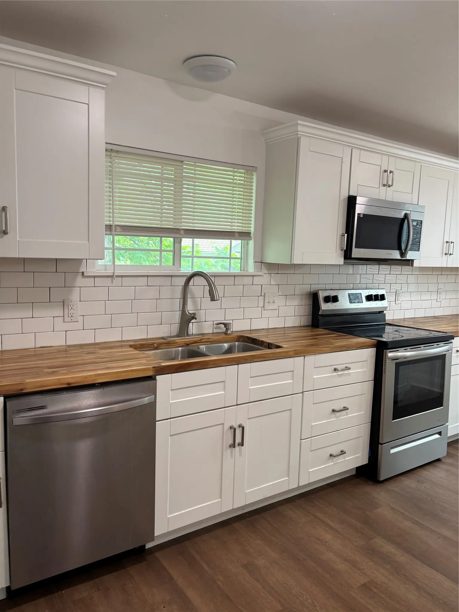 Modern kitchen featuring white shaker-style cabinetry, stainless steel appliances, wood-finish countertops, subway tile backsplash, and wood-finish flooring