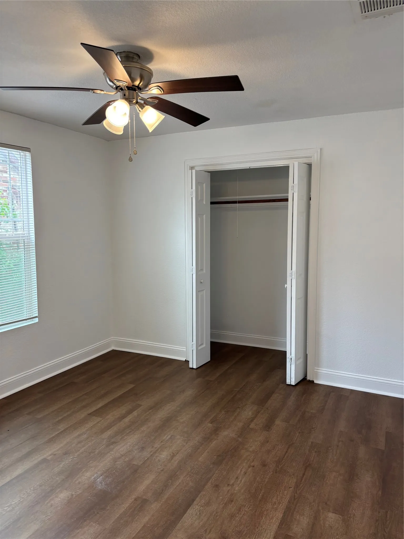 Bedroom featuring wood-finish flooring, a ceiling fan with integrated lighting, a window with horizontal blinds, and a bi-fold closet with an interior hanging rod