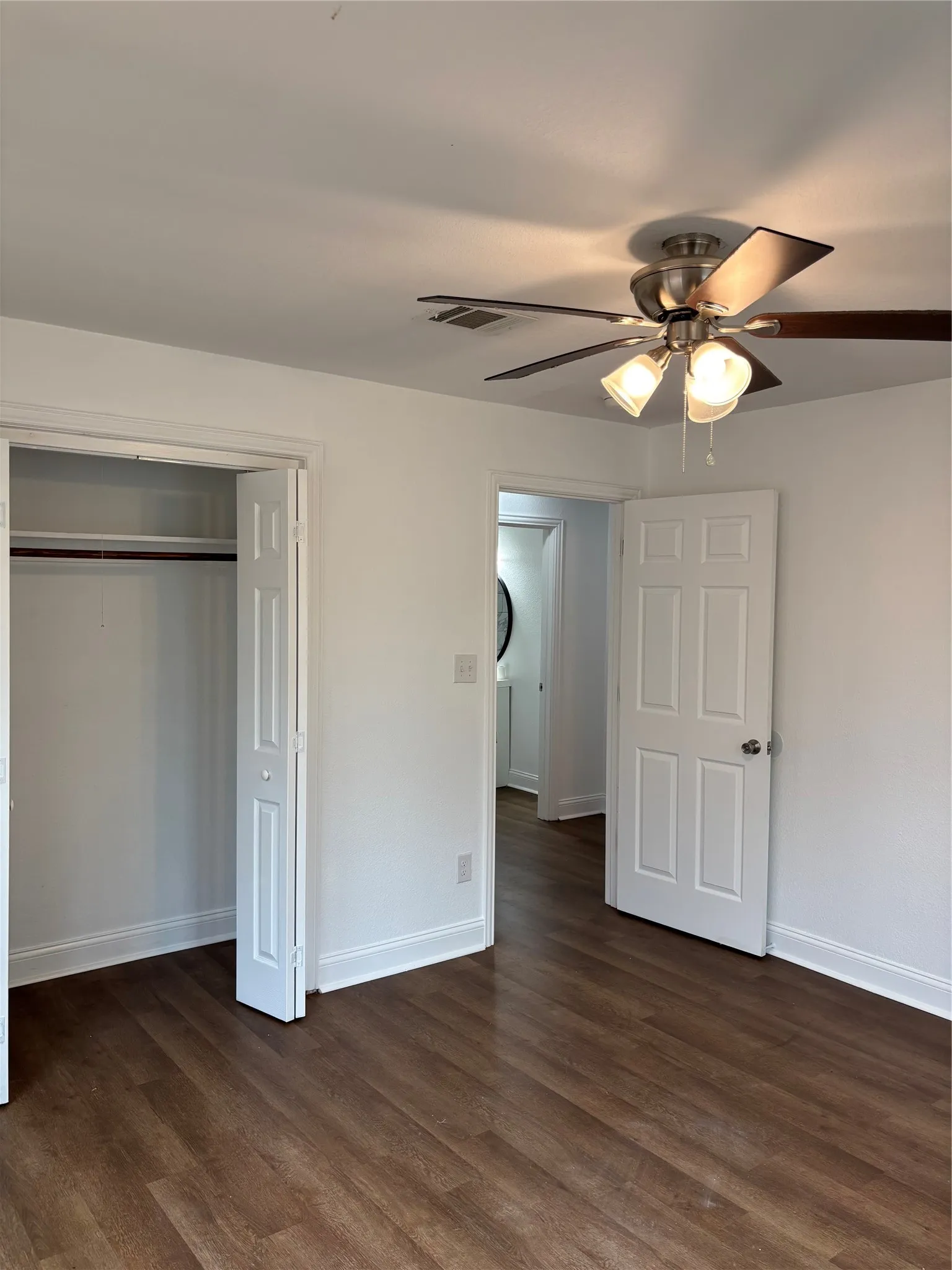 Spacious room featuring wood-finish flooring, crisp white walls, and a ceiling fan with integrated lighting