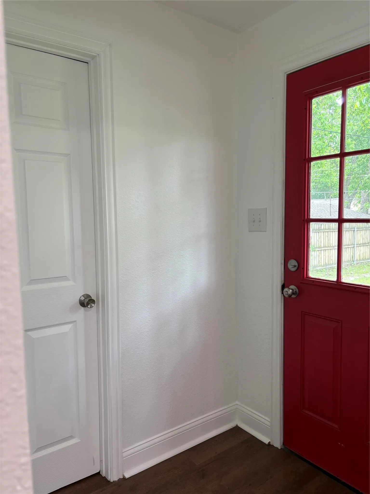 Vibrant red exterior door with multiple lites and dark hardware, complemented by white trim and wood-finish flooring