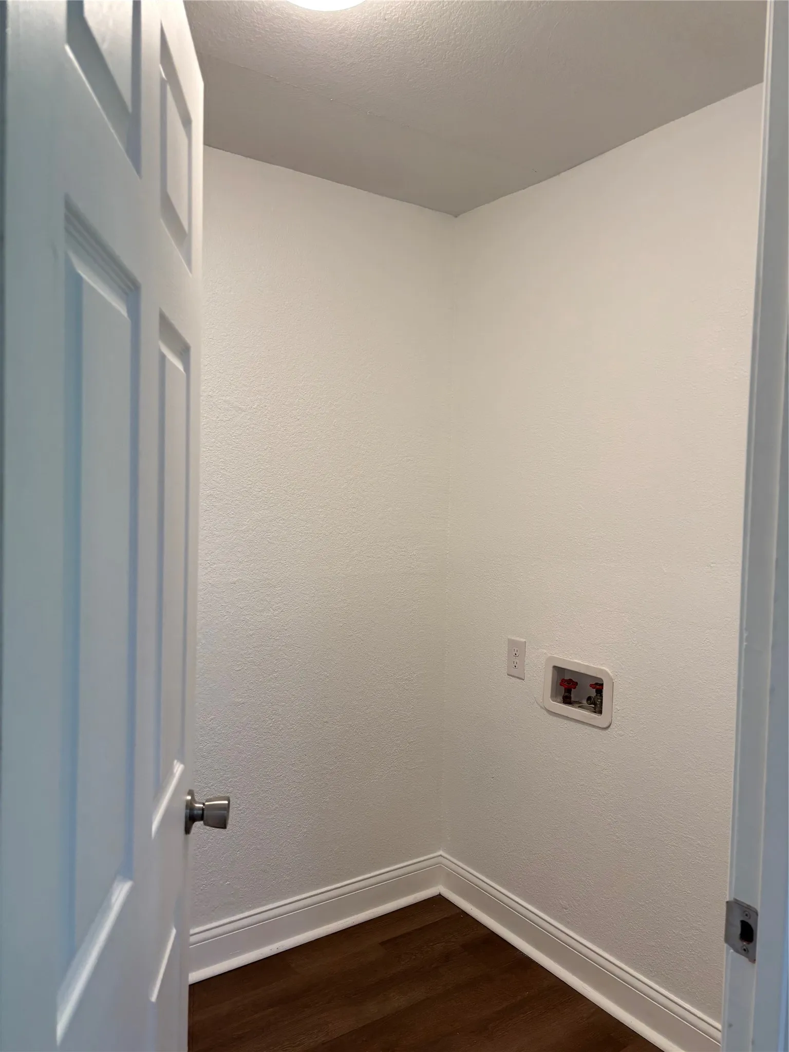 Dedicated laundry area featuring wood-finish flooring, white baseboards, and essential plumbing connections