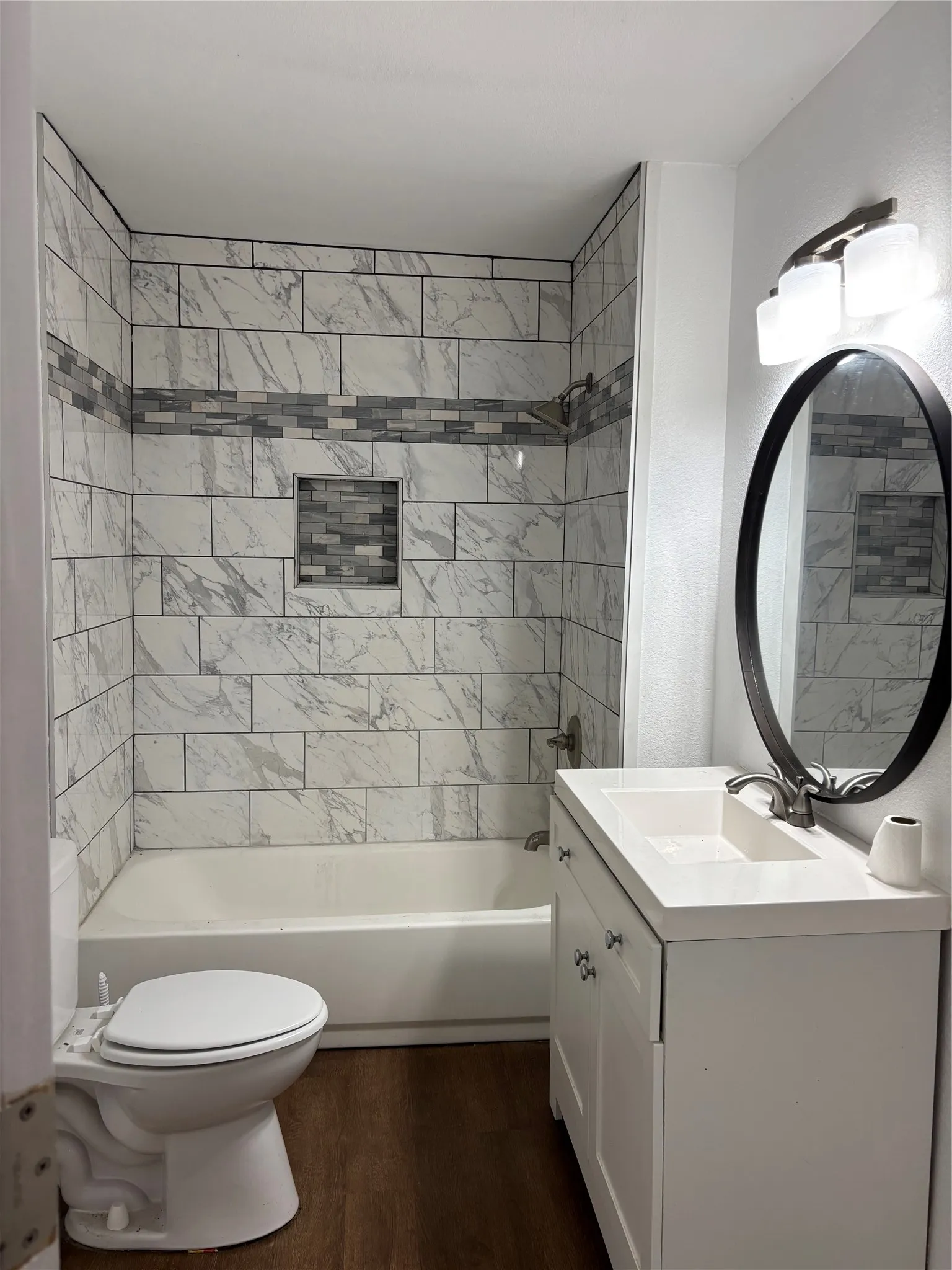 Bathroom featuring white subway tile surround with a decorative mosaic band and recessed niche