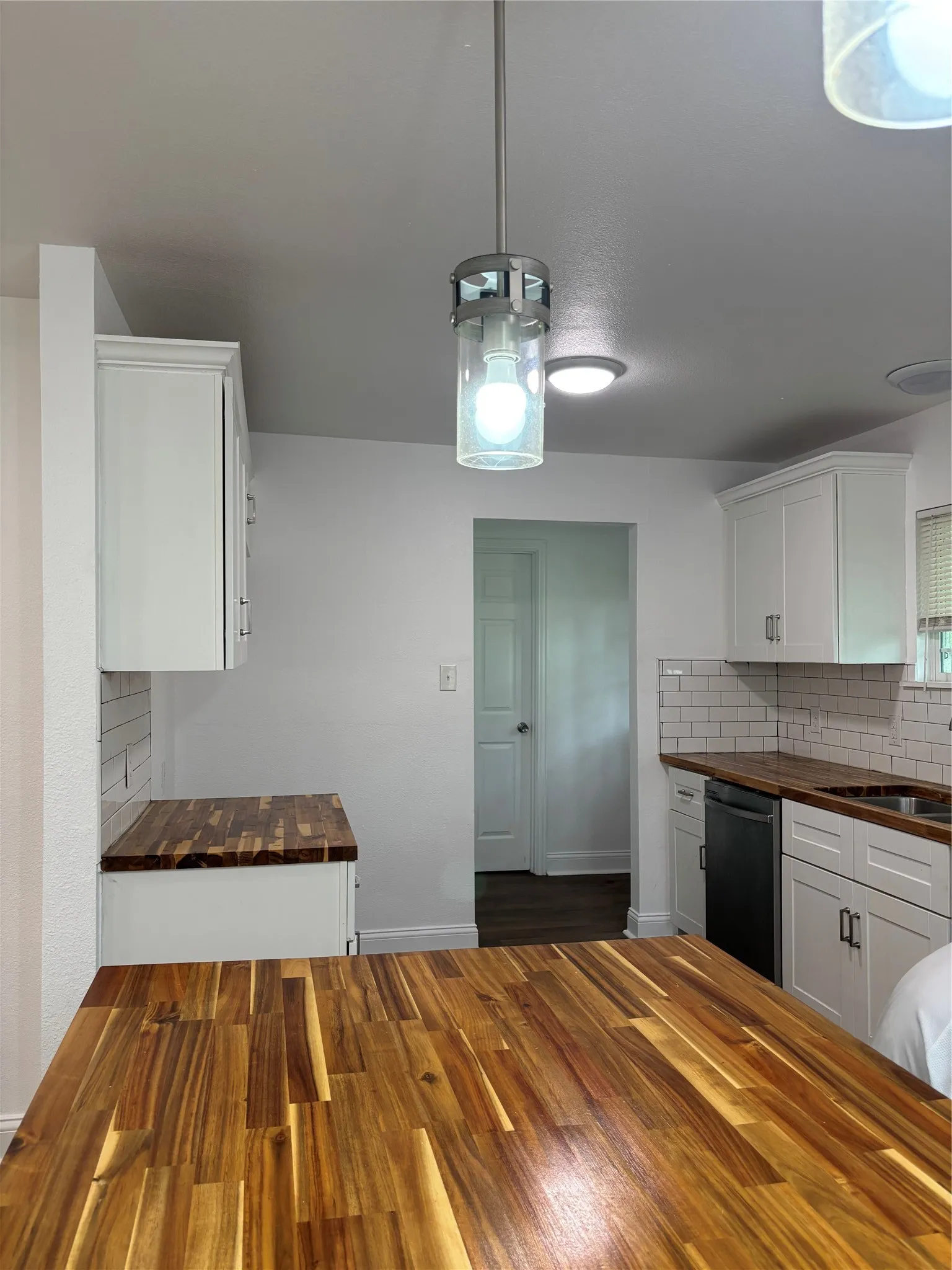 Kitchen featuring butcher block countertops, white shaker cabinetry, and a subway tile backsplash