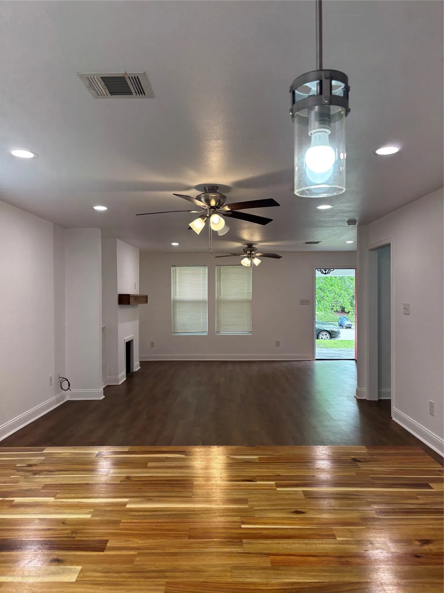 Open-concept living space with two distinct wood-finish flooring styles, recessed lighting, and multiple ceiling fans