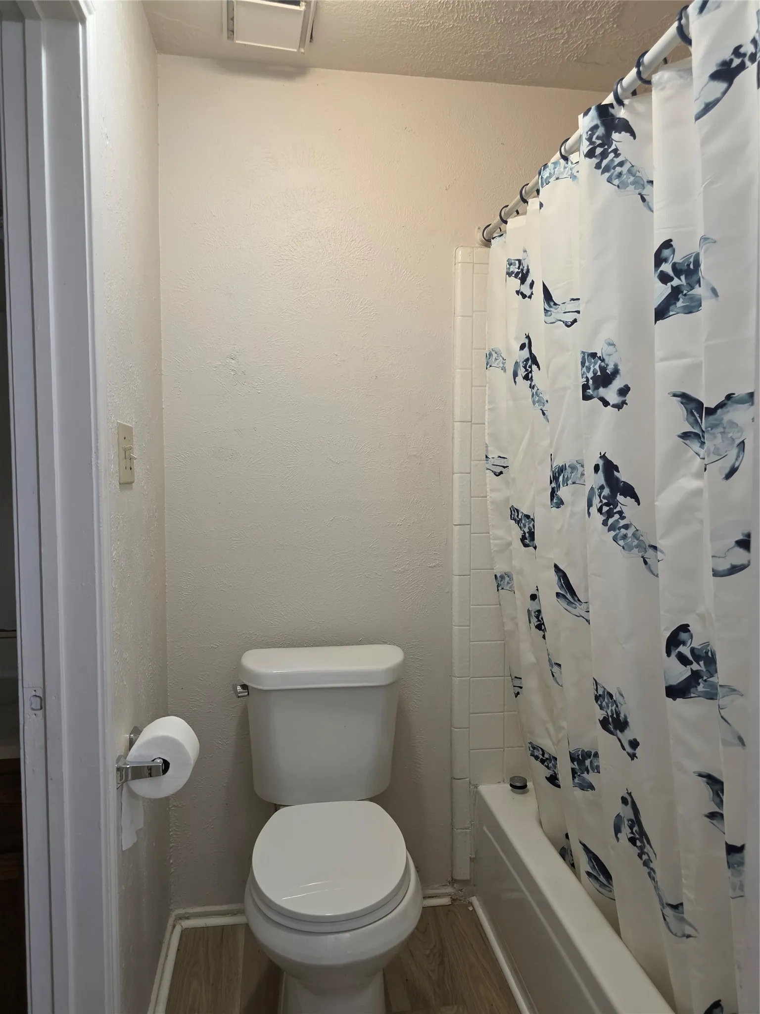 Bathroom featuring a white toilet, full-size bathtub, white tile surround, and wood-finish flooring