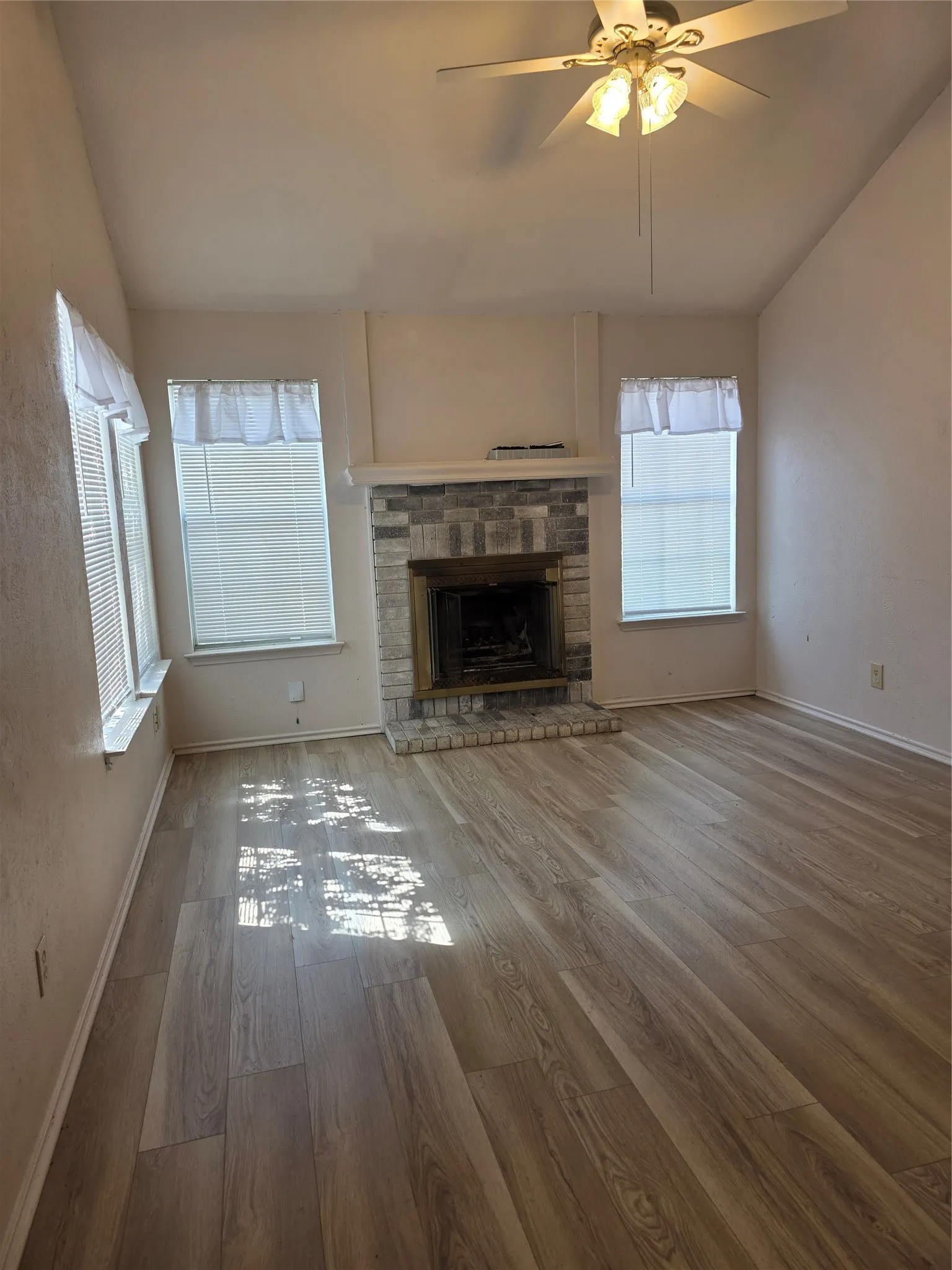 Vaulted ceilings with a ceiling fan, wood-finish flooring, and a stone-faced fireplace with a mantel