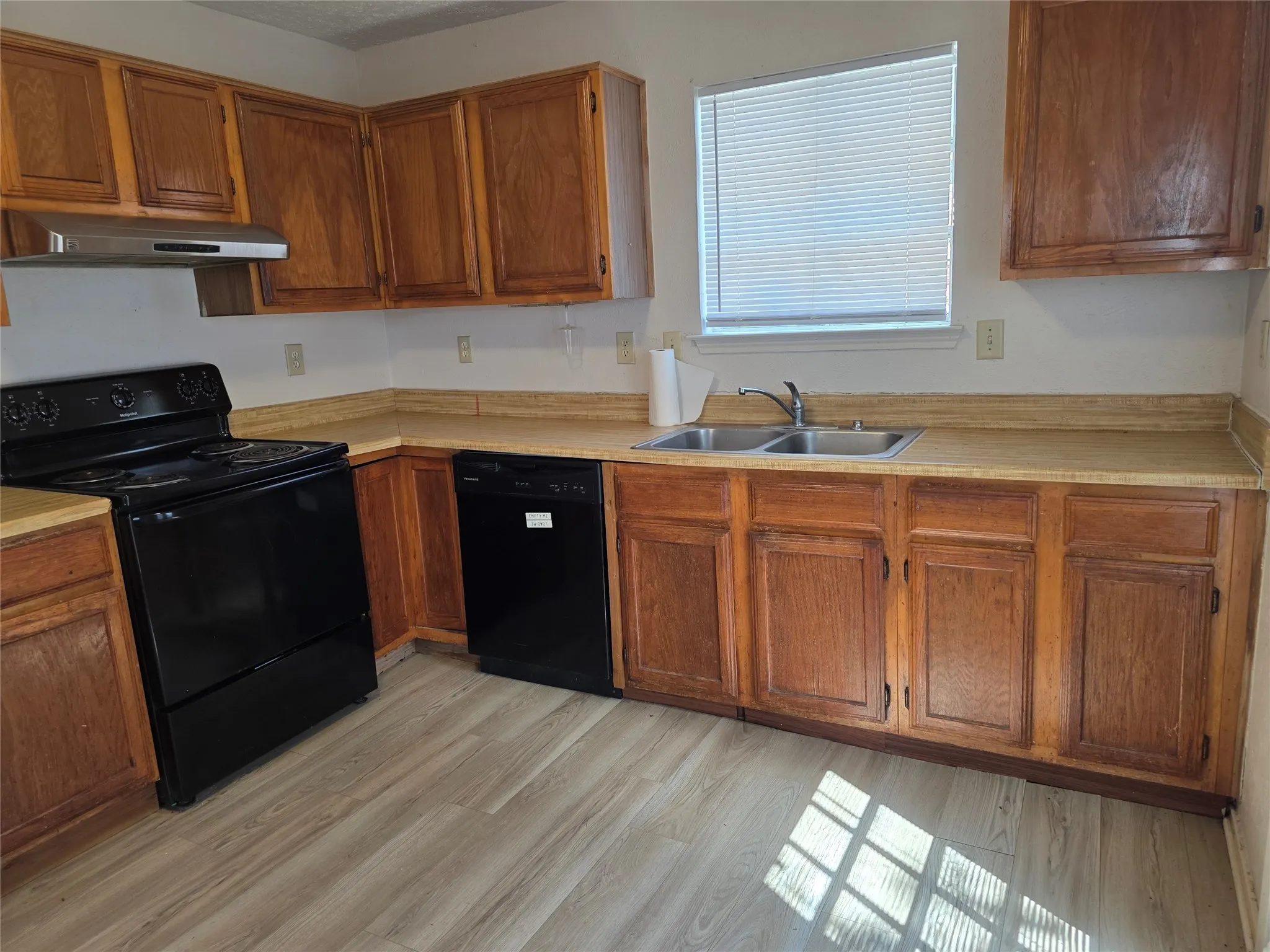 Wood-finish flooring, wood cabinetry, dual basin stainless steel sink, black electric range, and black dishwasher