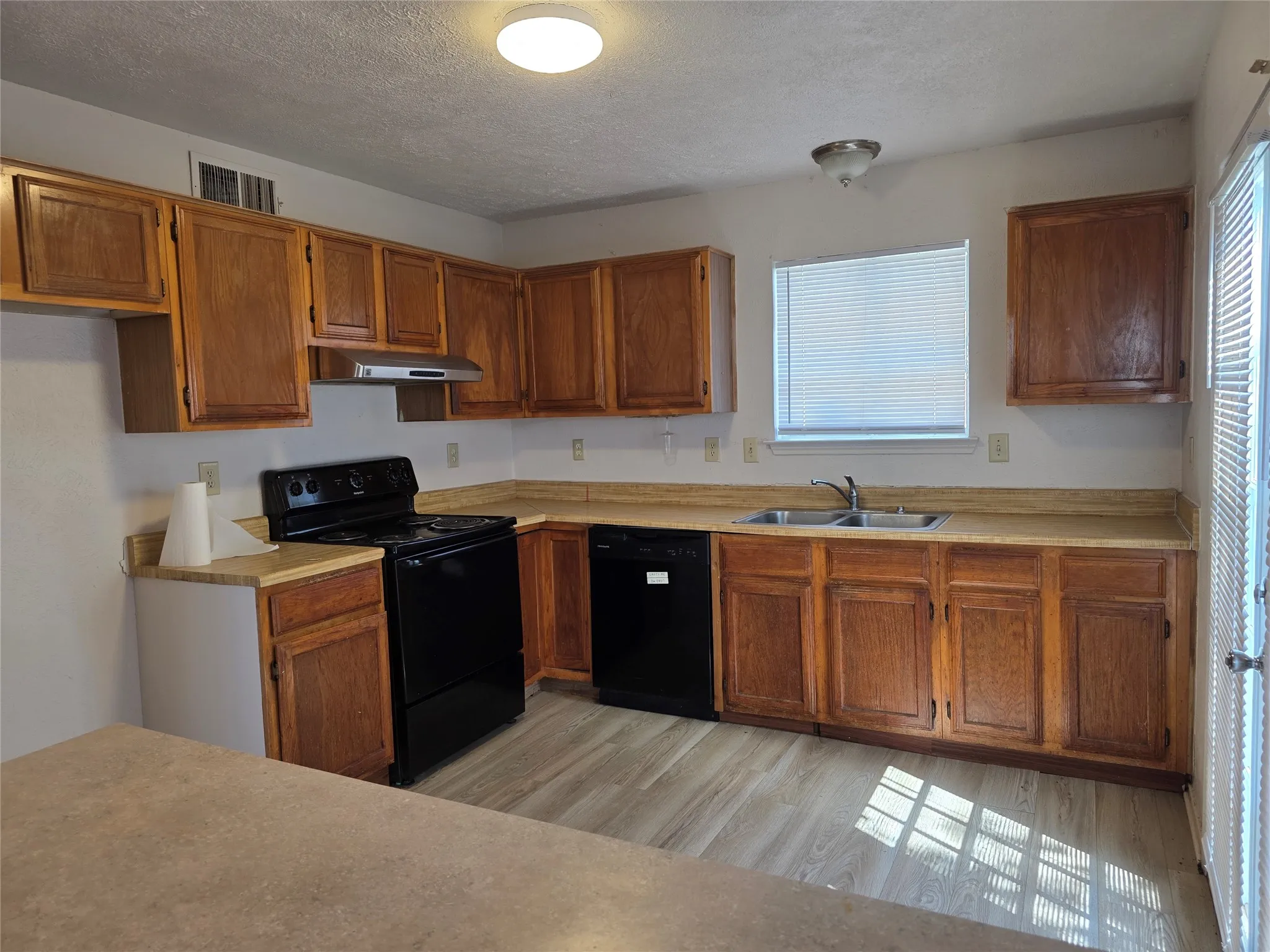 Kitchen featuring wood-finish cabinetry, black appliances, a double basin sink, and wood-finish flooring