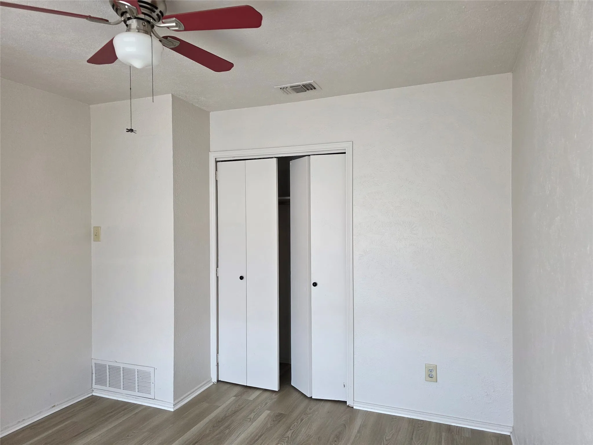Recessed bi-fold closet doors, ceiling fan with integrated lighting, wood-finish flooring, and white walls