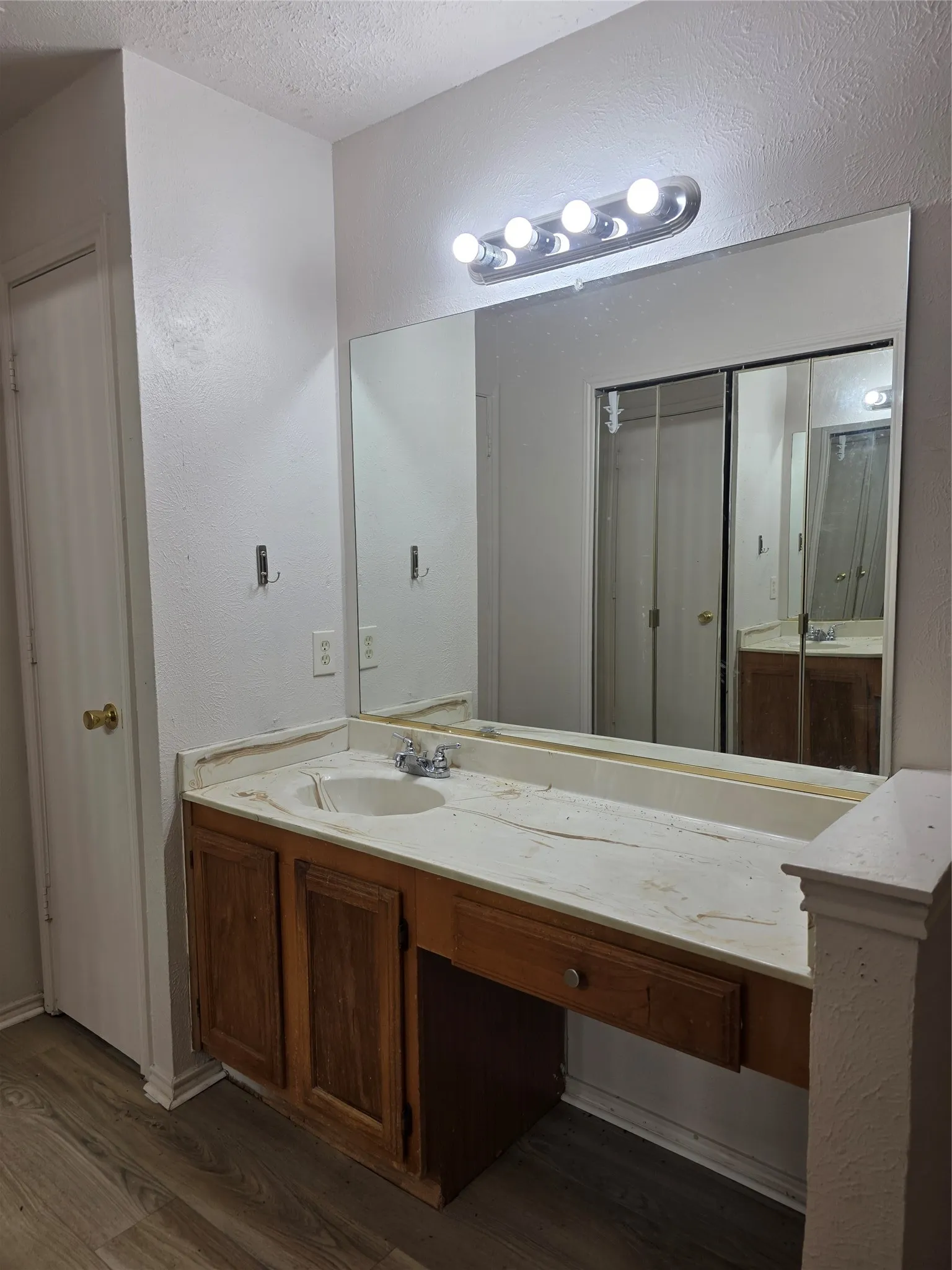 Vanity with a built-in sink, wood-finish cabinetry, full-width mirror, and overhead strip lighting