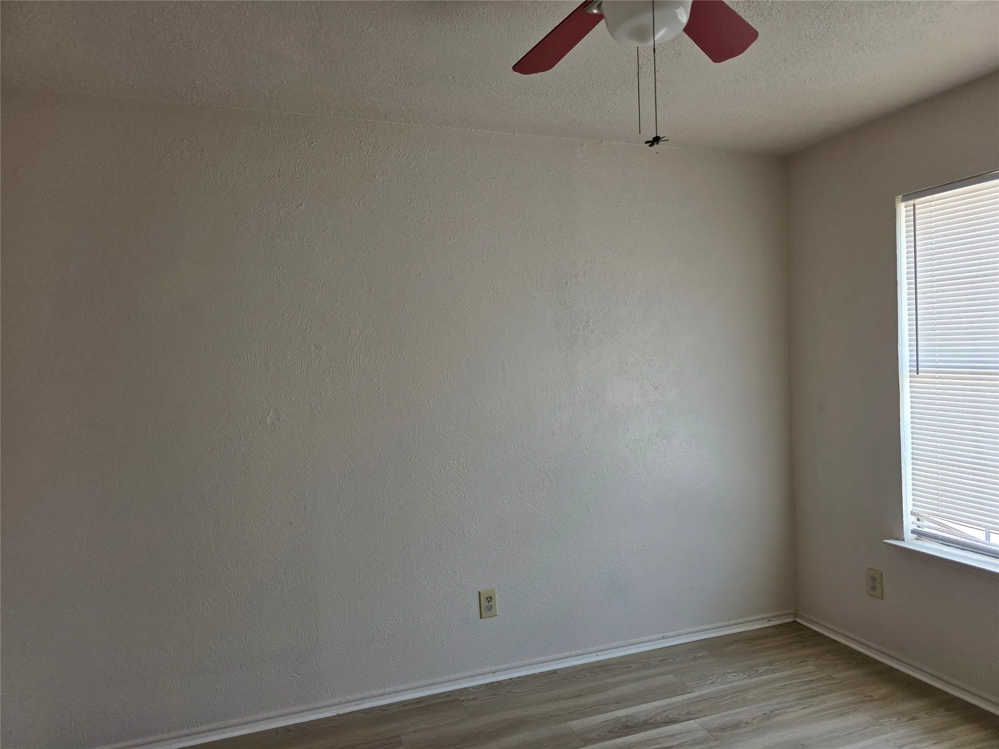 Wood-finish flooring, ceiling fan, window with blinds, and neutral wall tones