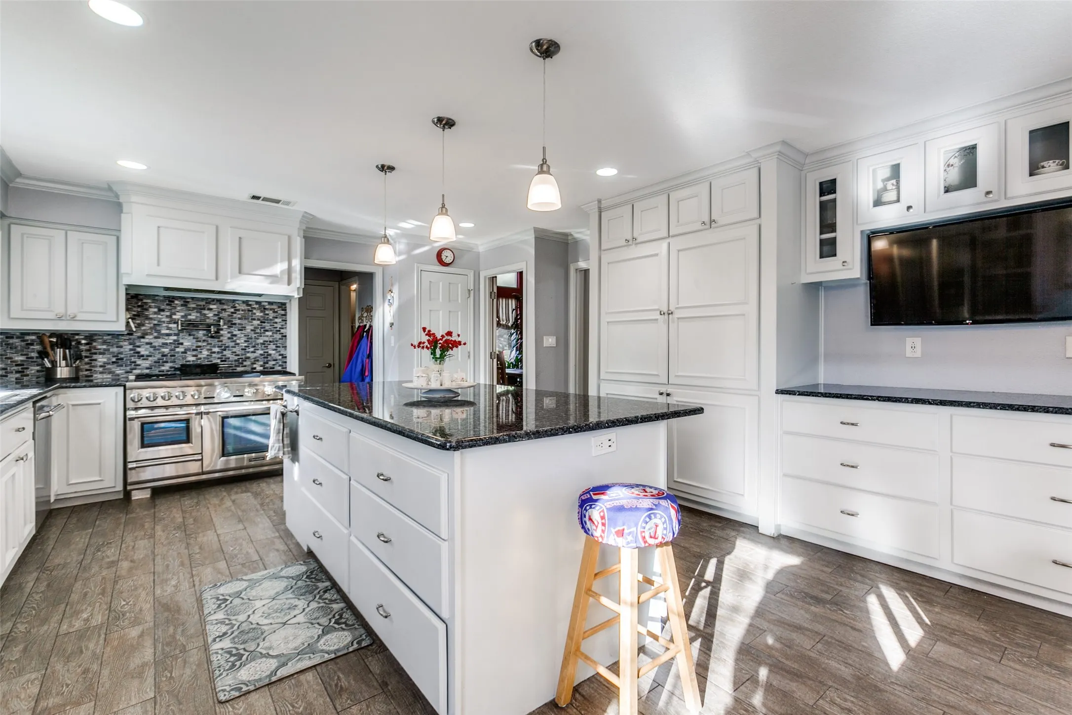 Kitchen featuring a large central island with a dark countertop, white cabinetry, a mosaic tile backsplash, stainless steel range with double ovens, and wood-finish flooring