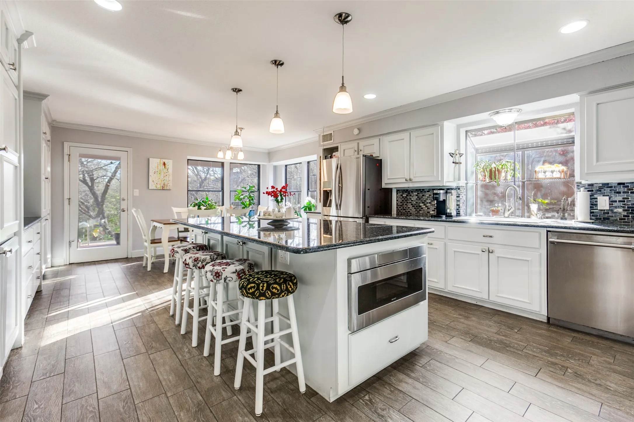 Kitchen featuring an oversized island with pendant lighting, integrated stainless steel microwave, extensive white cabinetry, and stainless steel appliances