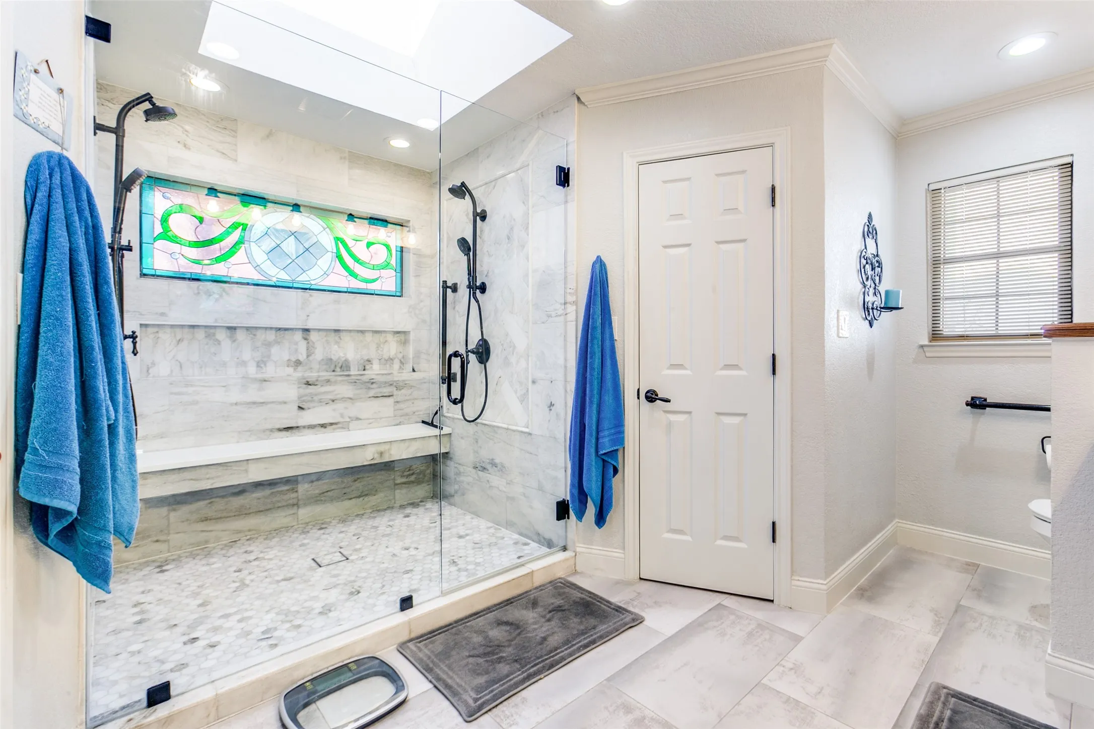 Frameless glass shower enclosure featuring a built-in bench, dual showerheads, and a decorative stained-glass accent