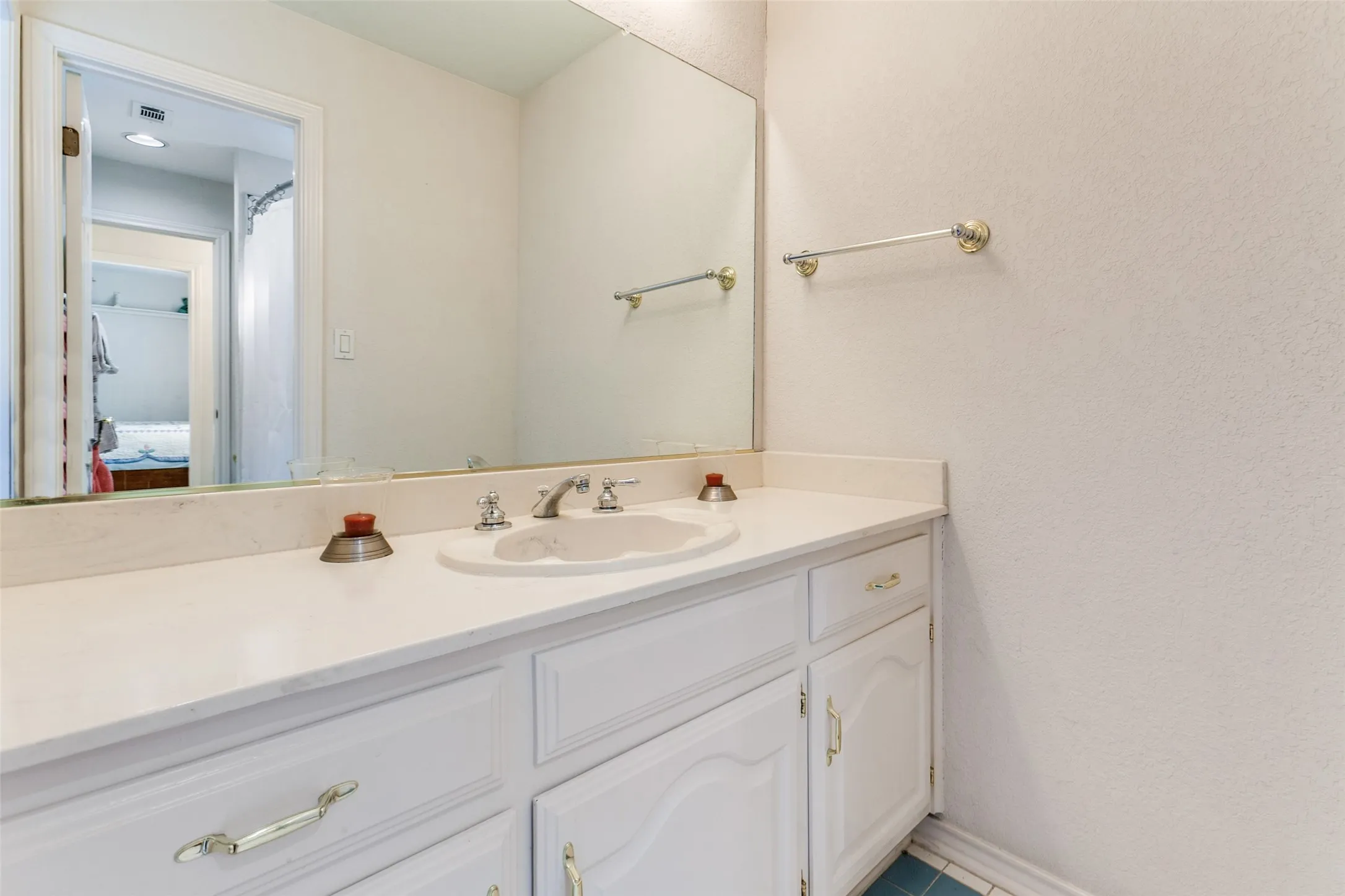 Bathroom vanity featuring a single basin, white countertop, and white cabinetry with brass-toned hardware