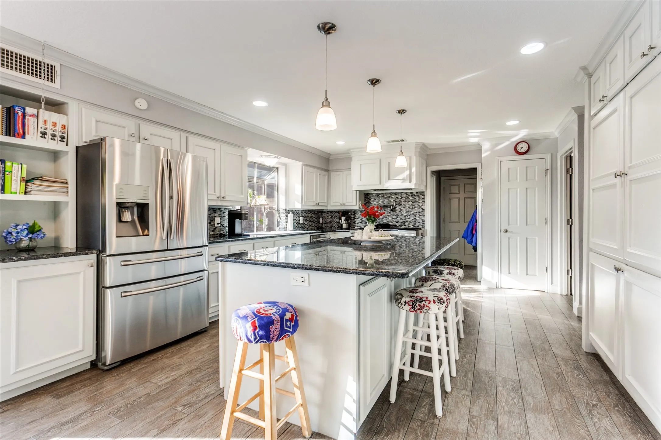 Spacious kitchen featuring an extended island with pendant lighting, white cabinetry, dark stone countertops, stainless steel appliances, and wood-finish flooring