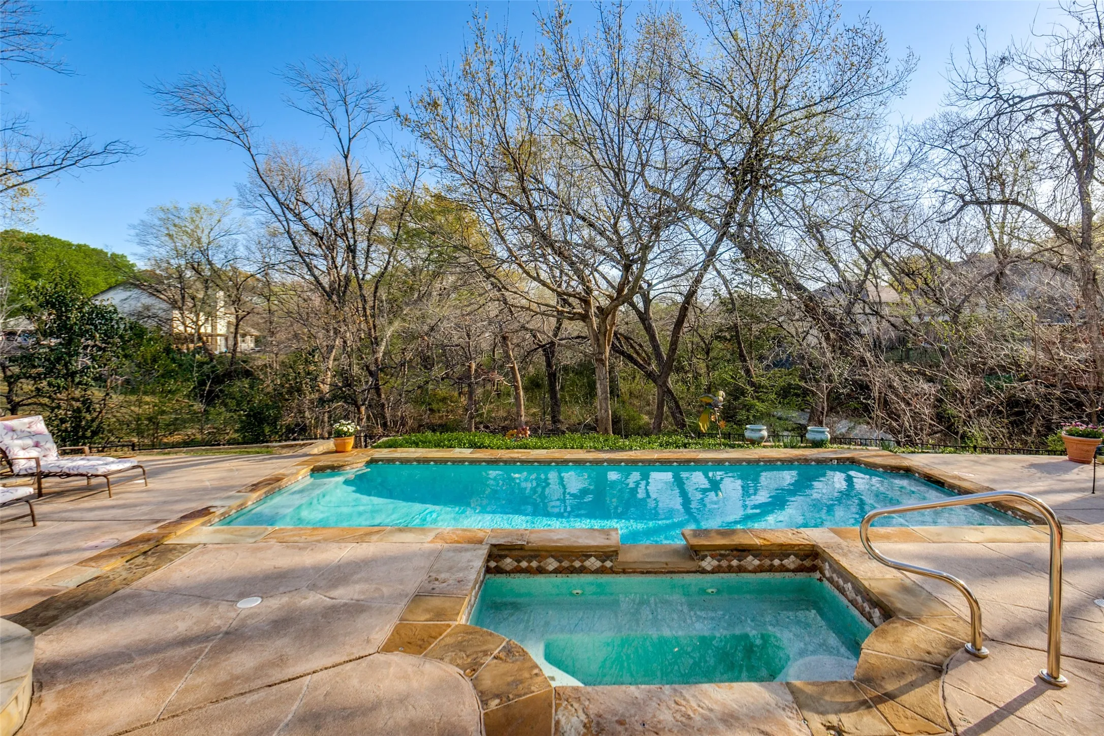 Outdoor swimming pool featuring a connected spa, surrounding stone coping, concrete decking, and a stainless steel grab rail