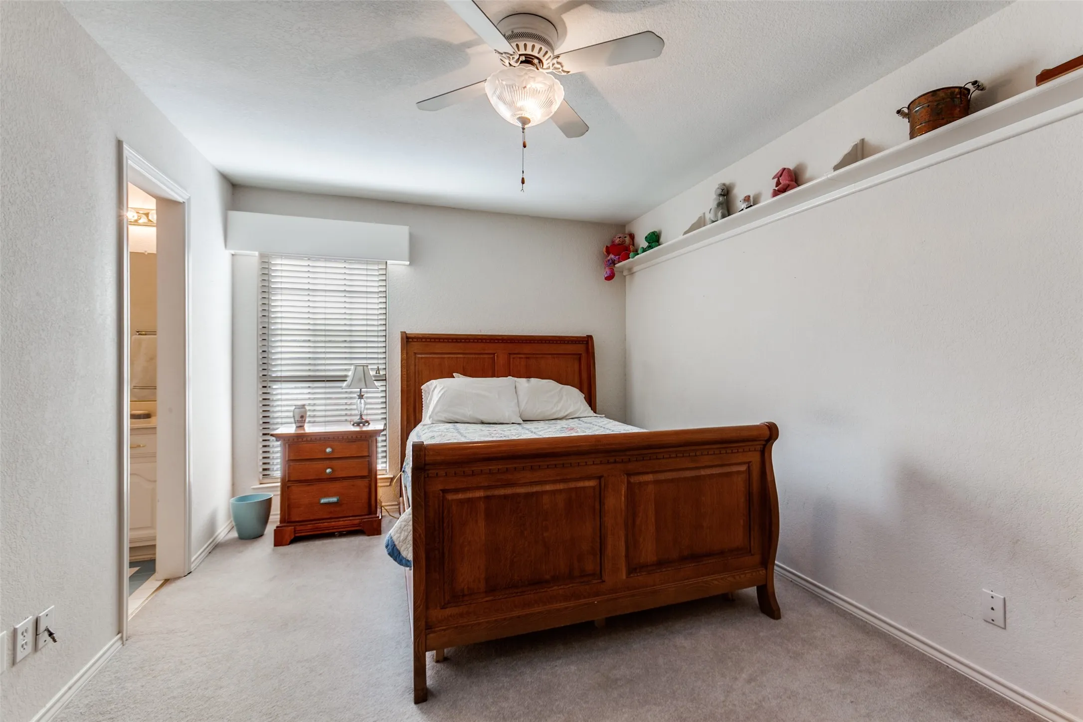Carpeted bedroom featuring a ceiling fan with integrated lighting, a window with horizontal blinds, and a built-in wall shelf