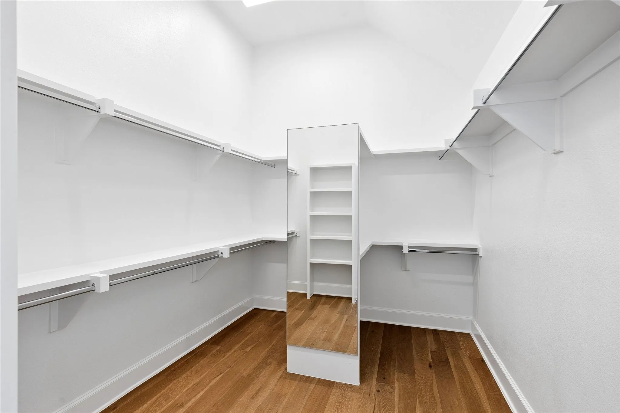 Walk-in closet featuring wood-finish flooring, crisp white walls, extensive shelving, integrated hanging rods, and a full-length mirror