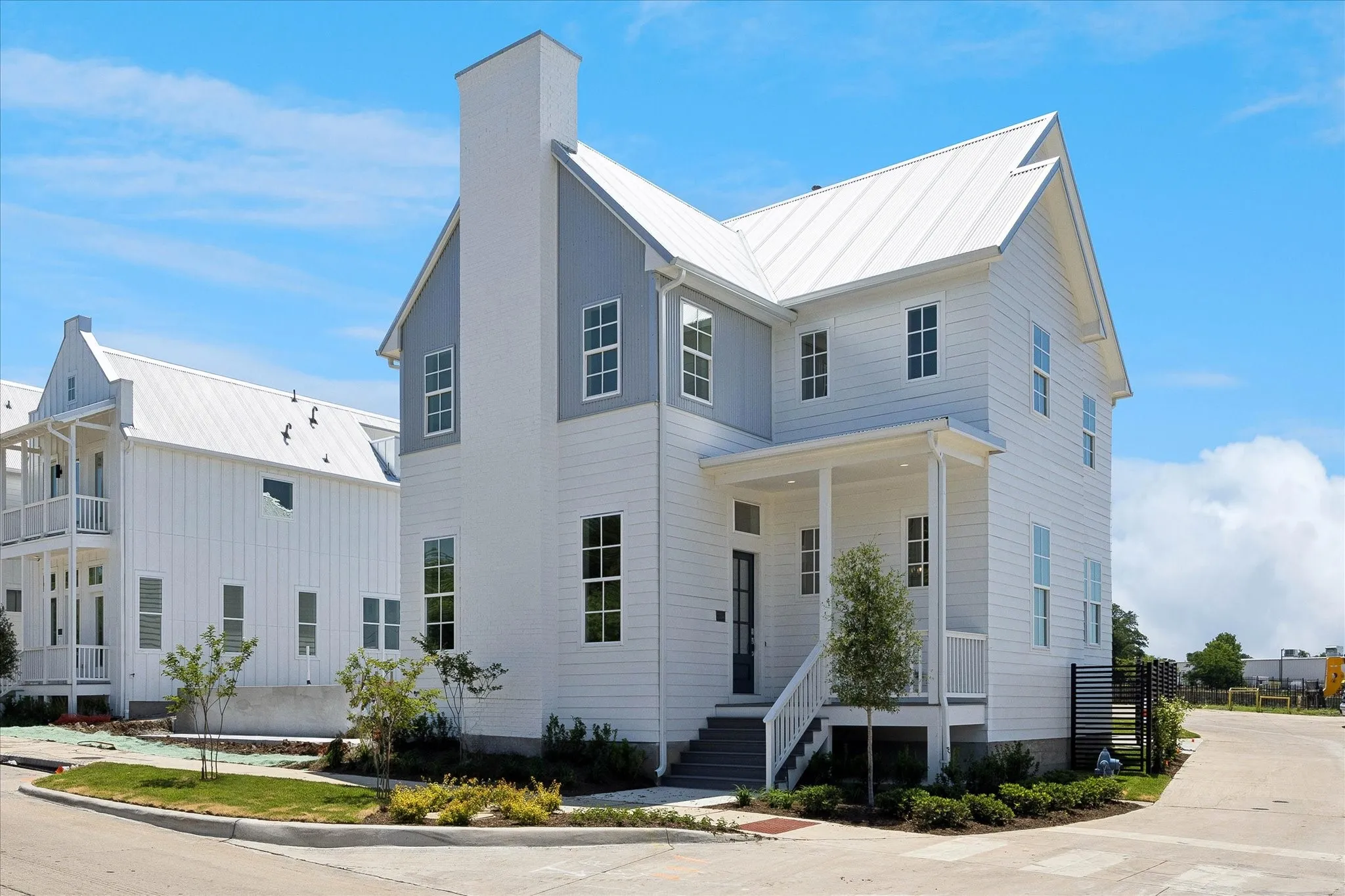 Modern farmhouse architecture featuring a white exterior with blue accents, a standing seam metal roof, a covered entry porch, and multiple window arrays