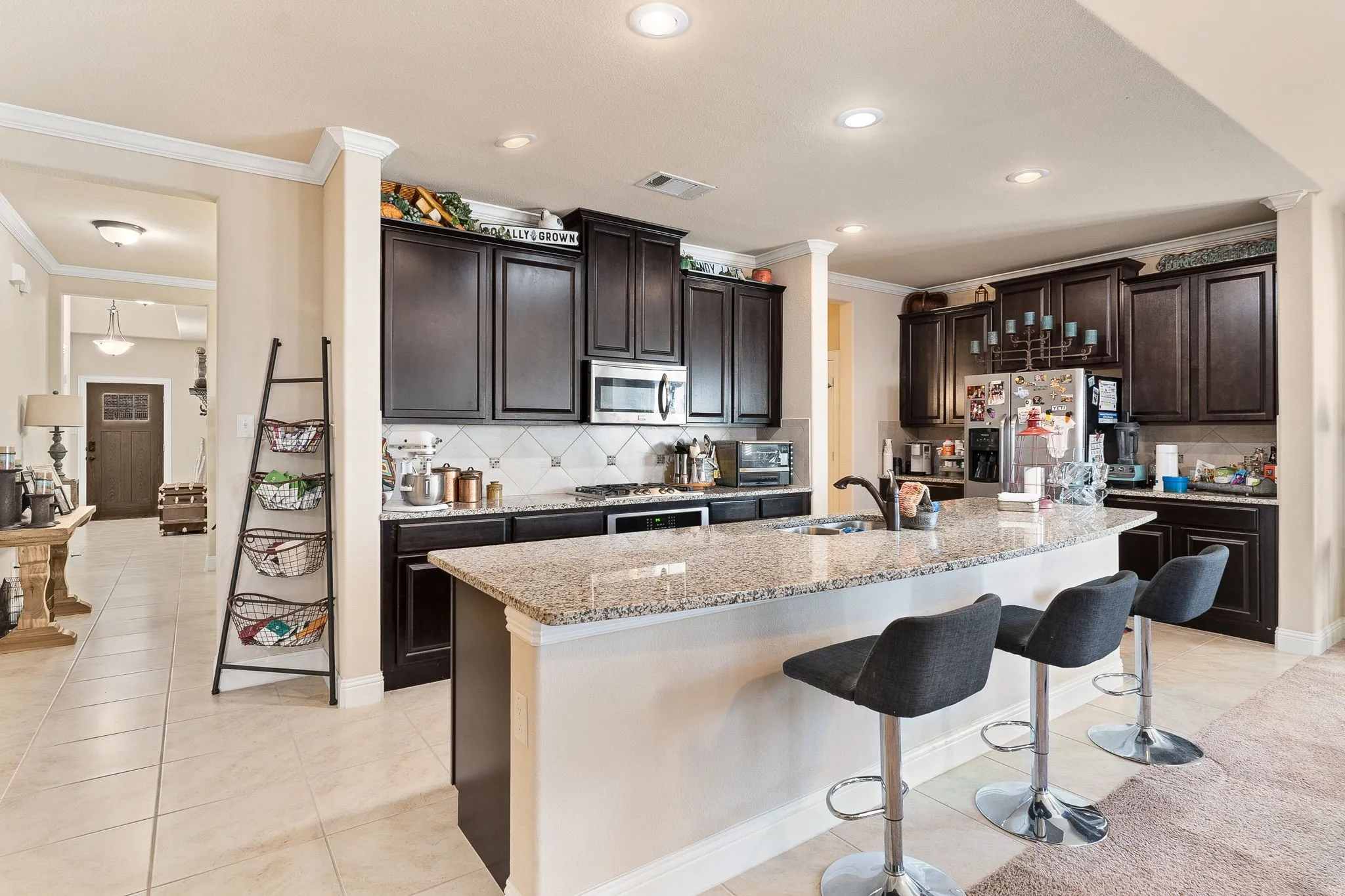 Kitchen with dark brown cabinetry, stainless steel appliances, a center island with sink, and light stone​​‌​​​​‌​​‌‌​‌‌​​​‌‌​‌​‌​‌​​​‌​​ counters