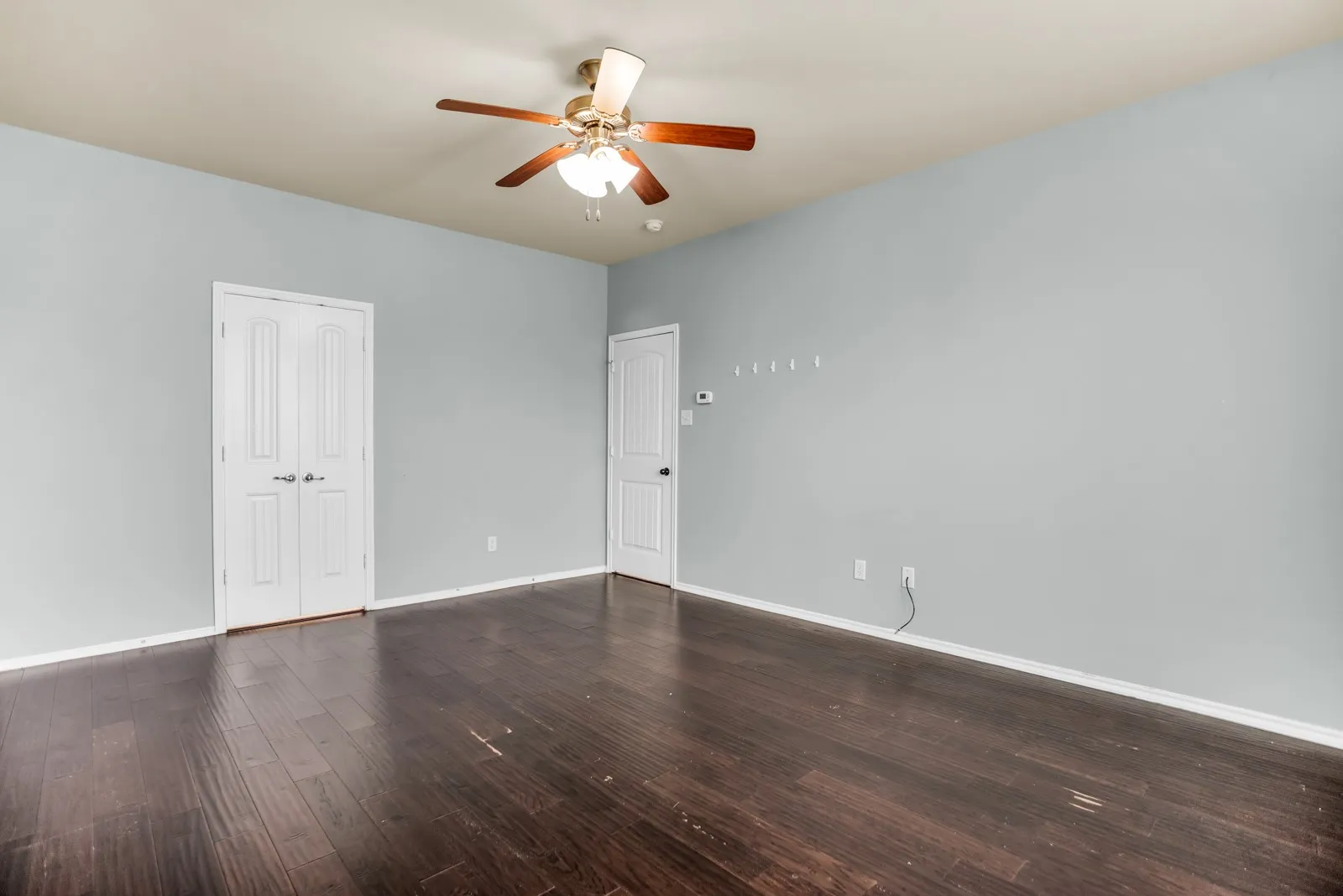 Spacious room featuring dark wood-finish flooring and light gray painted walls