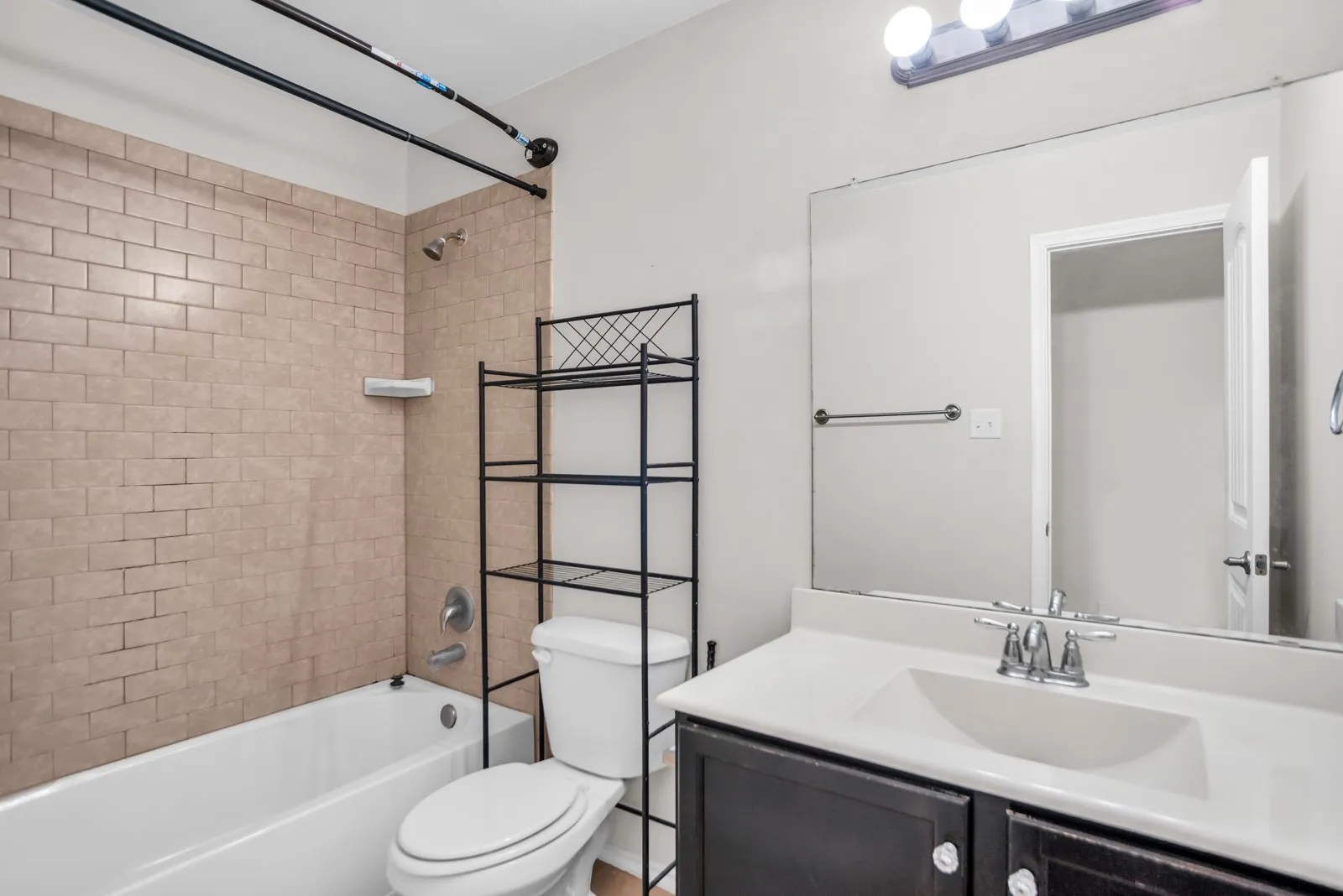 Bathroom featuring a tub/shower combination with subway tile surround, a white toilet, and a vanity with a white countertop and dark cabinetry