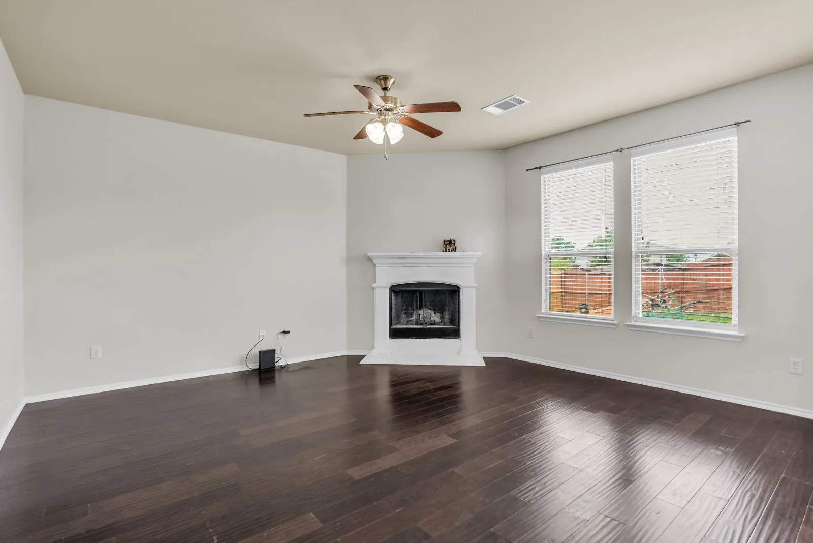 Living area featuring a white mantel fireplace, dark wood-finish flooring, and a ceiling fan with integrated lighting