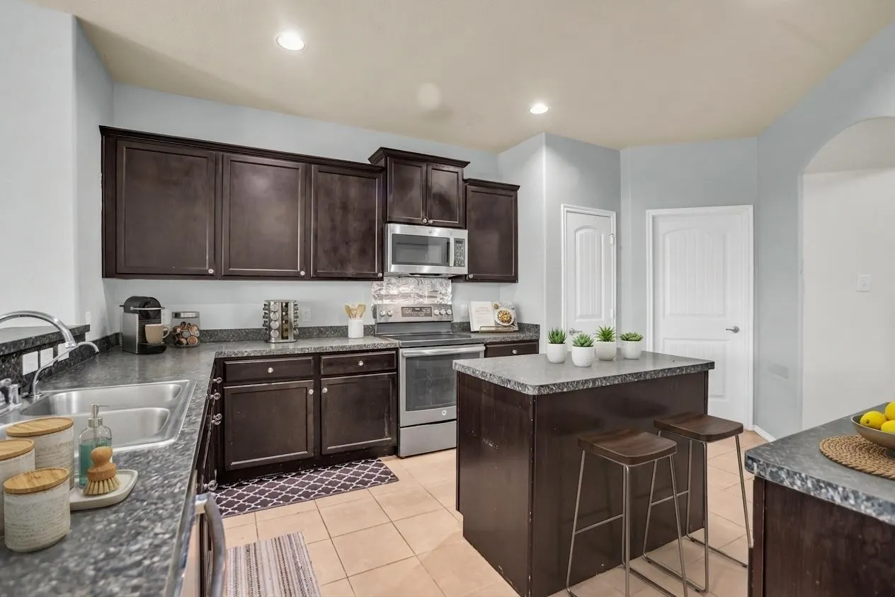 Virtual Staging -Kitchen featuring dark wood cabinetry, granite-finish countertops, stainless steel appliances, a center island with seating, and ceramic tile flooring
