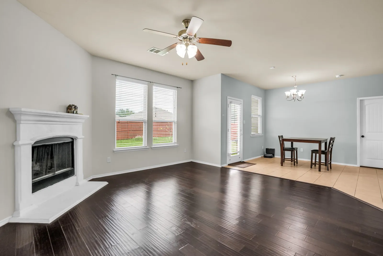 Spacious room featuring dark wood-finish flooring, a white fireplace with an angled hearth, and abundant natural light from multiple windows