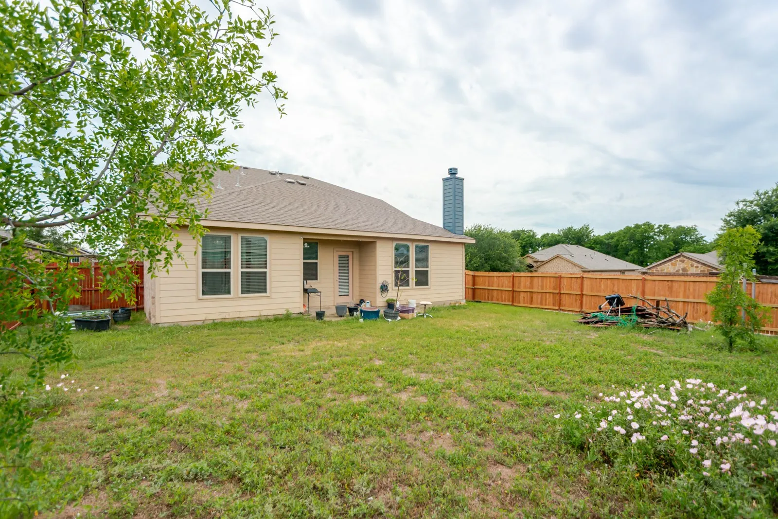 Expansive backyard featuring a privacy fence, established shrubbery, and a single-story residence with a patio door and multiple windows