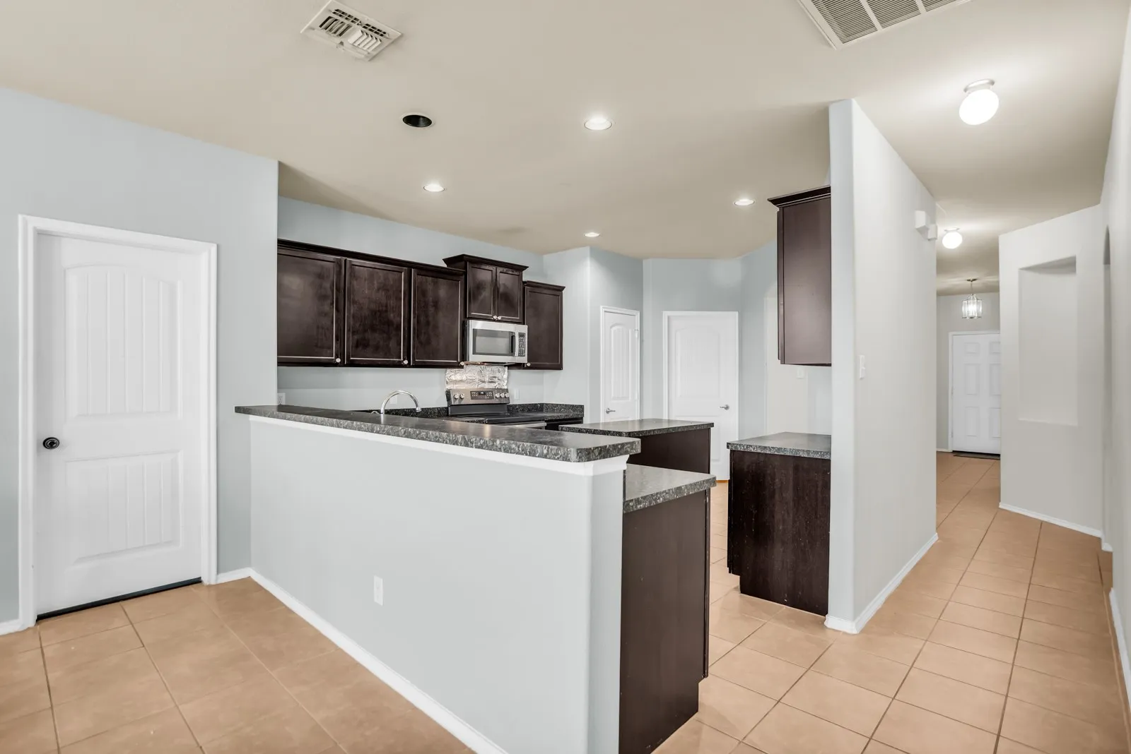 Kitchen featuring dark wood cabinetry, light-toned countertops, and stainless steel appliances including a microwave and range