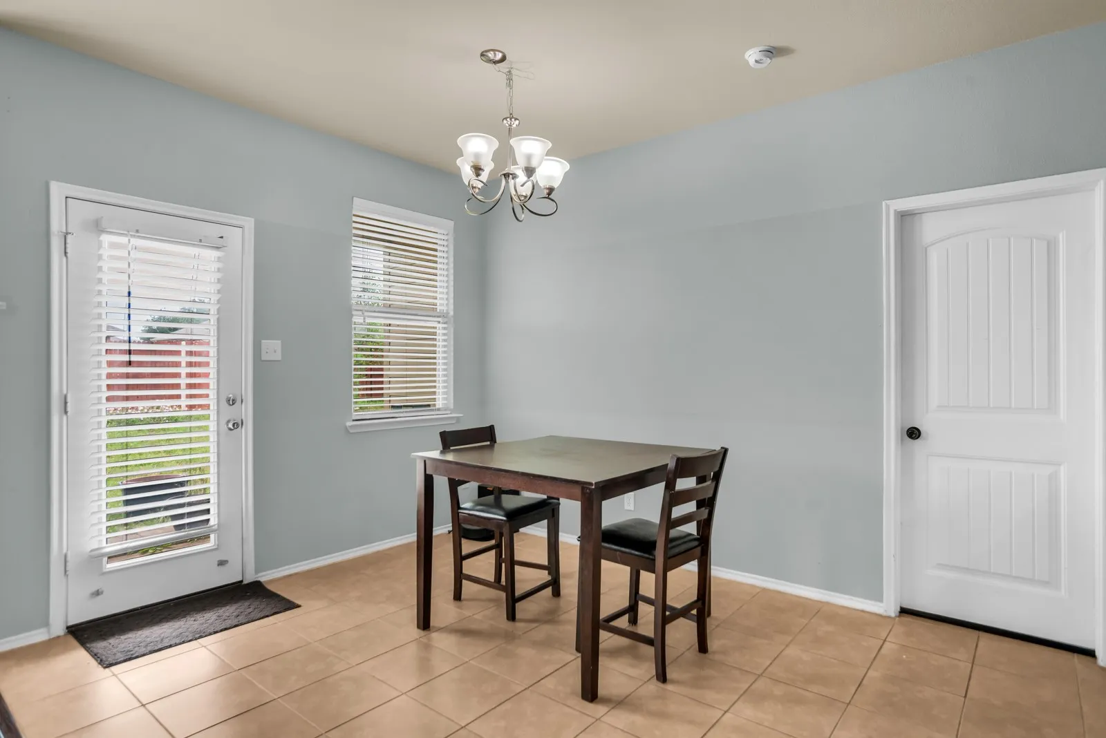 Dining area featuring tile flooring, a glass-paned door with integrated blinds, and an overhead chandelier