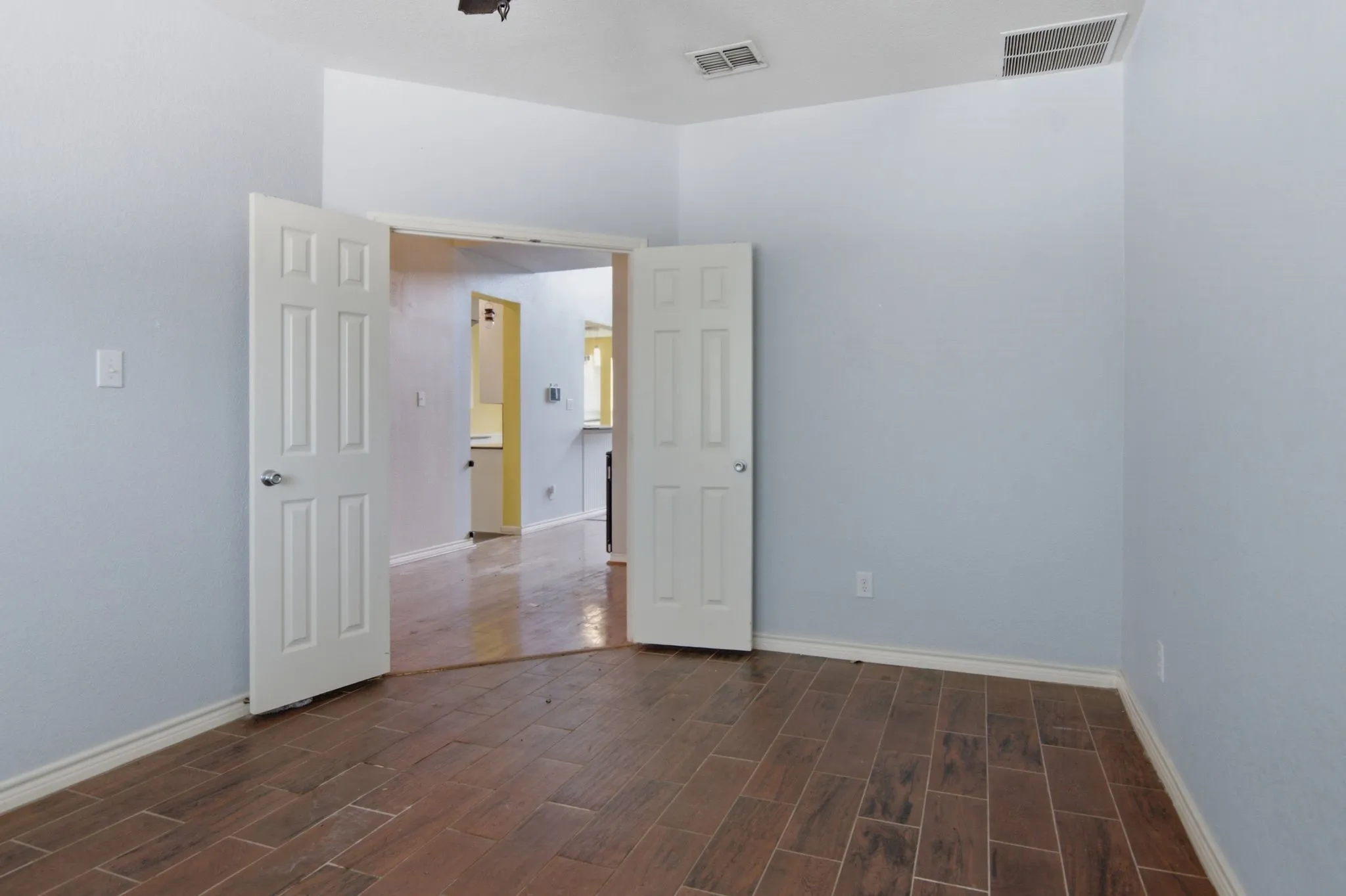 Room featuring wood-finish tile flooring, light blue wall paint, white trim, and white paneled double doors