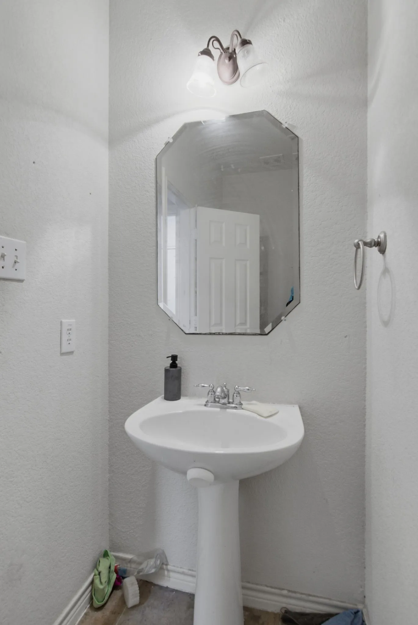 Pedestal sink with chrome faucet, octagonal mirror, and wall-mounted vanity lighting