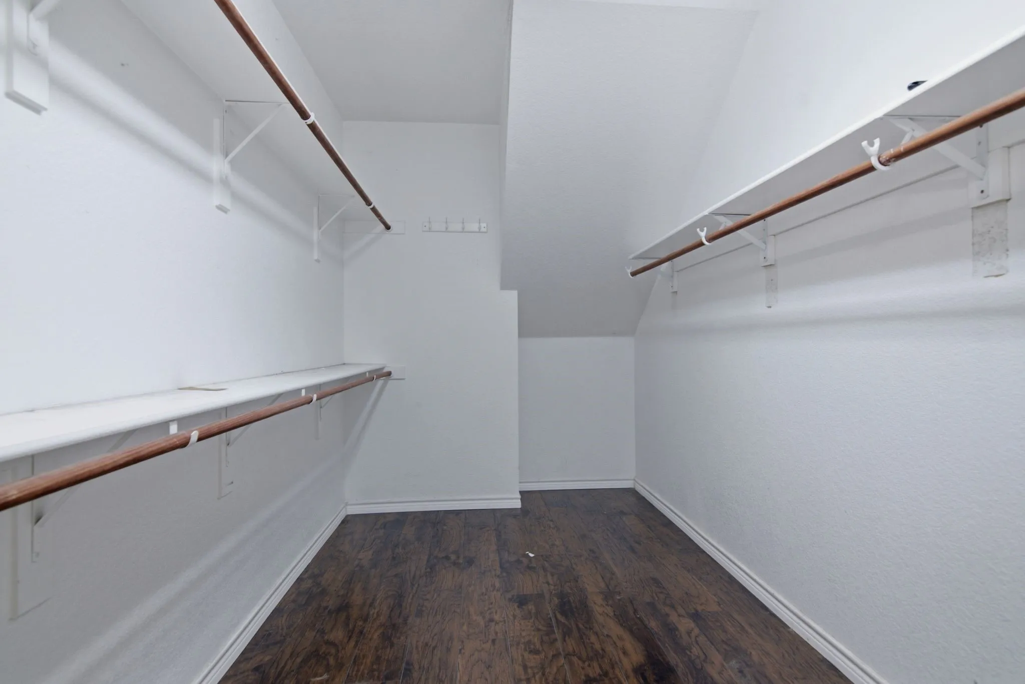 Walk-in closet featuring wood-finish flooring, white walls, multiple storage shelves, and hanging rods