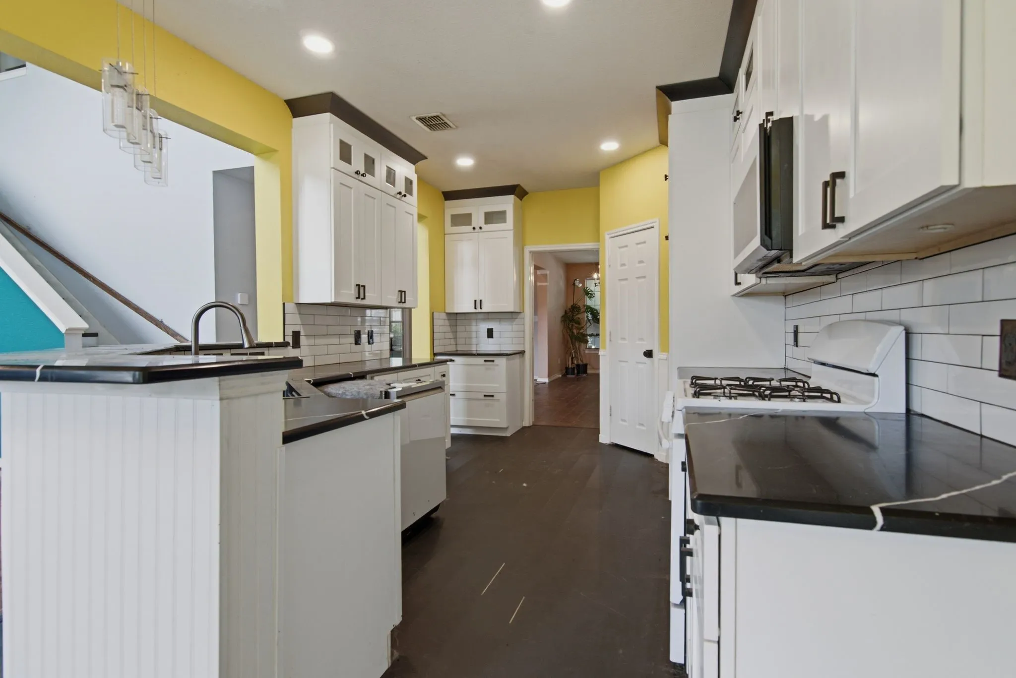 Contemporary kitchen featuring dark countertops, white cabinetry, a subway tile backsplash, and dark wood-finish flooring