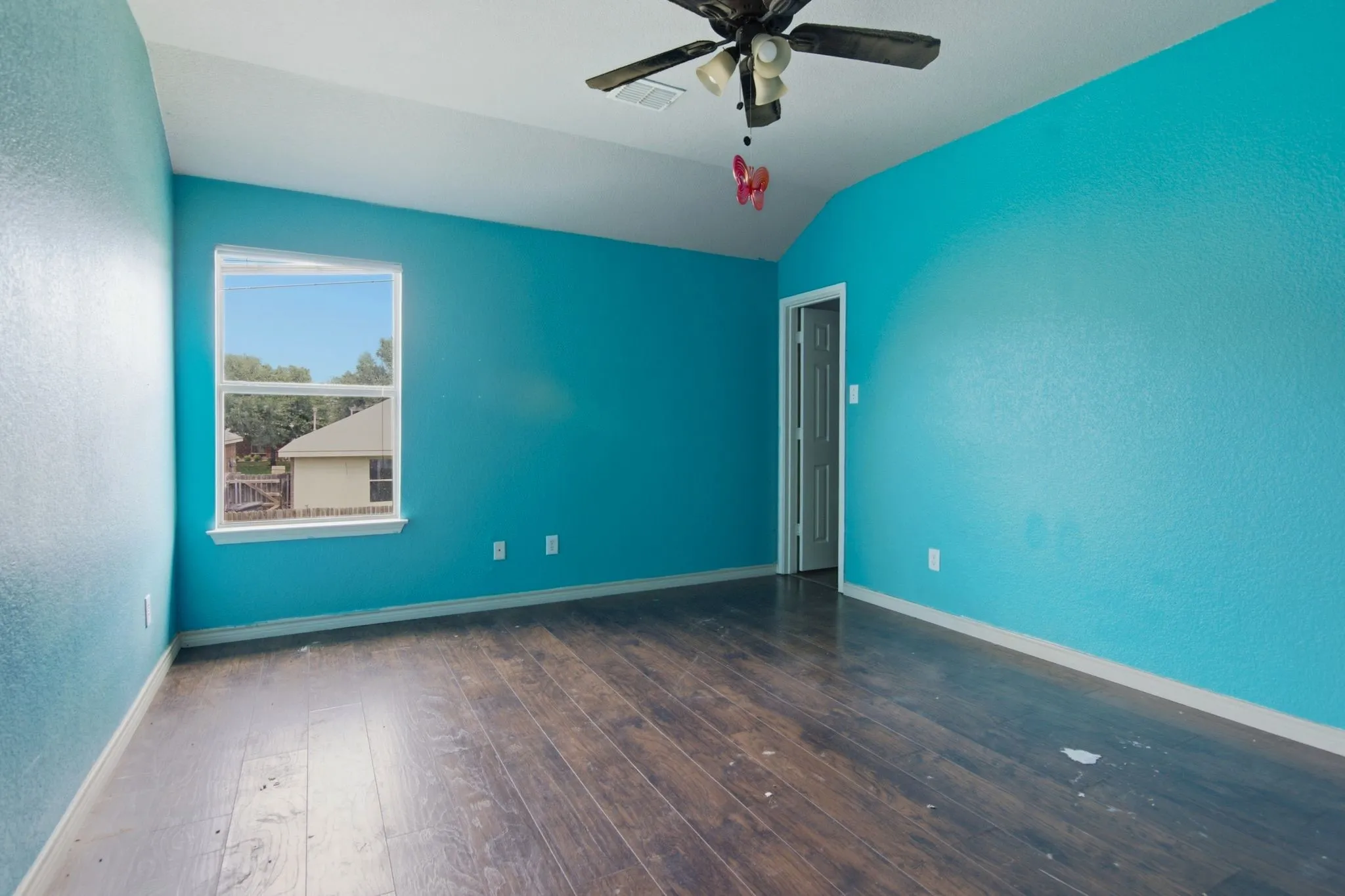 Room featuring rich wood-finish flooring, vibrant blue textured walls, and a window with white trim