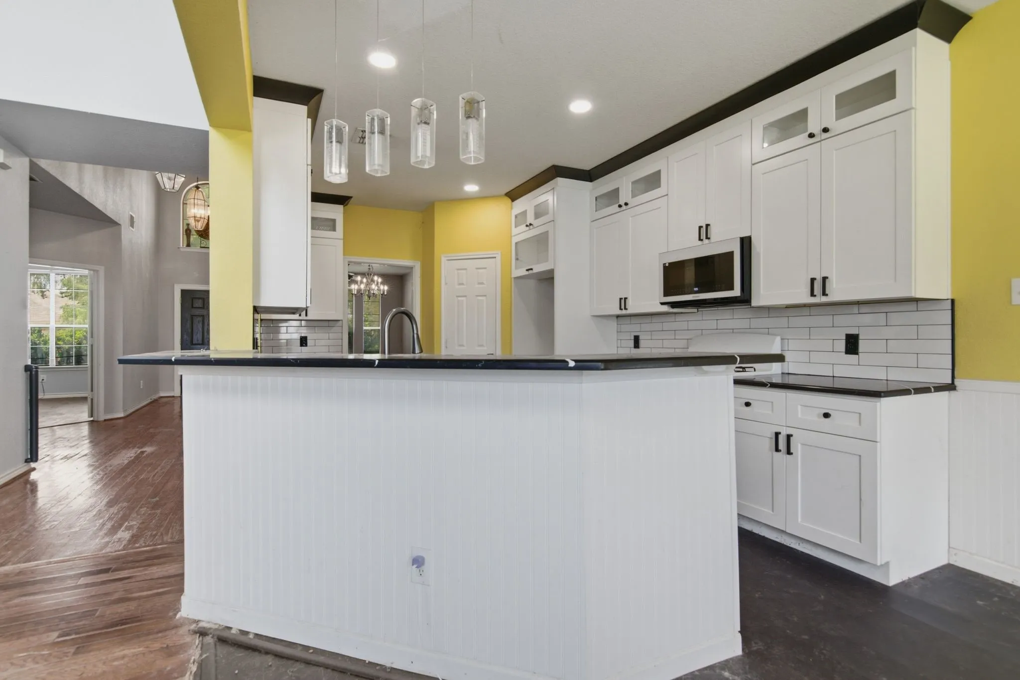 Kitchen featuring white shaker cabinetry, black countertops, stainless steel microwave, subway tile backsplash, and beadboard paneling