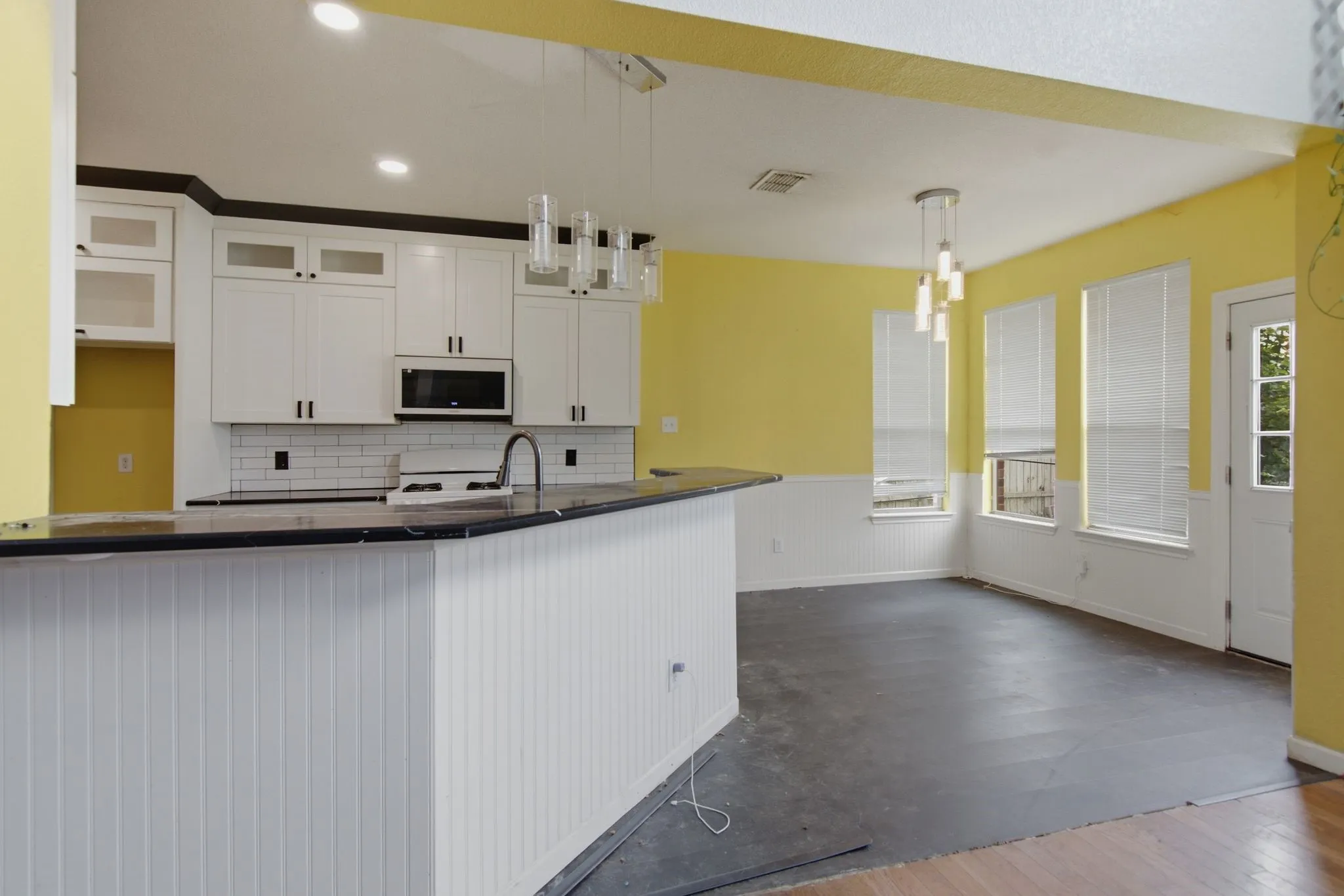 Kitchen and dining area featuring white cabinetry, dark countertops, a subway tile backsplash, and a breakfast bar with beadboard paneling