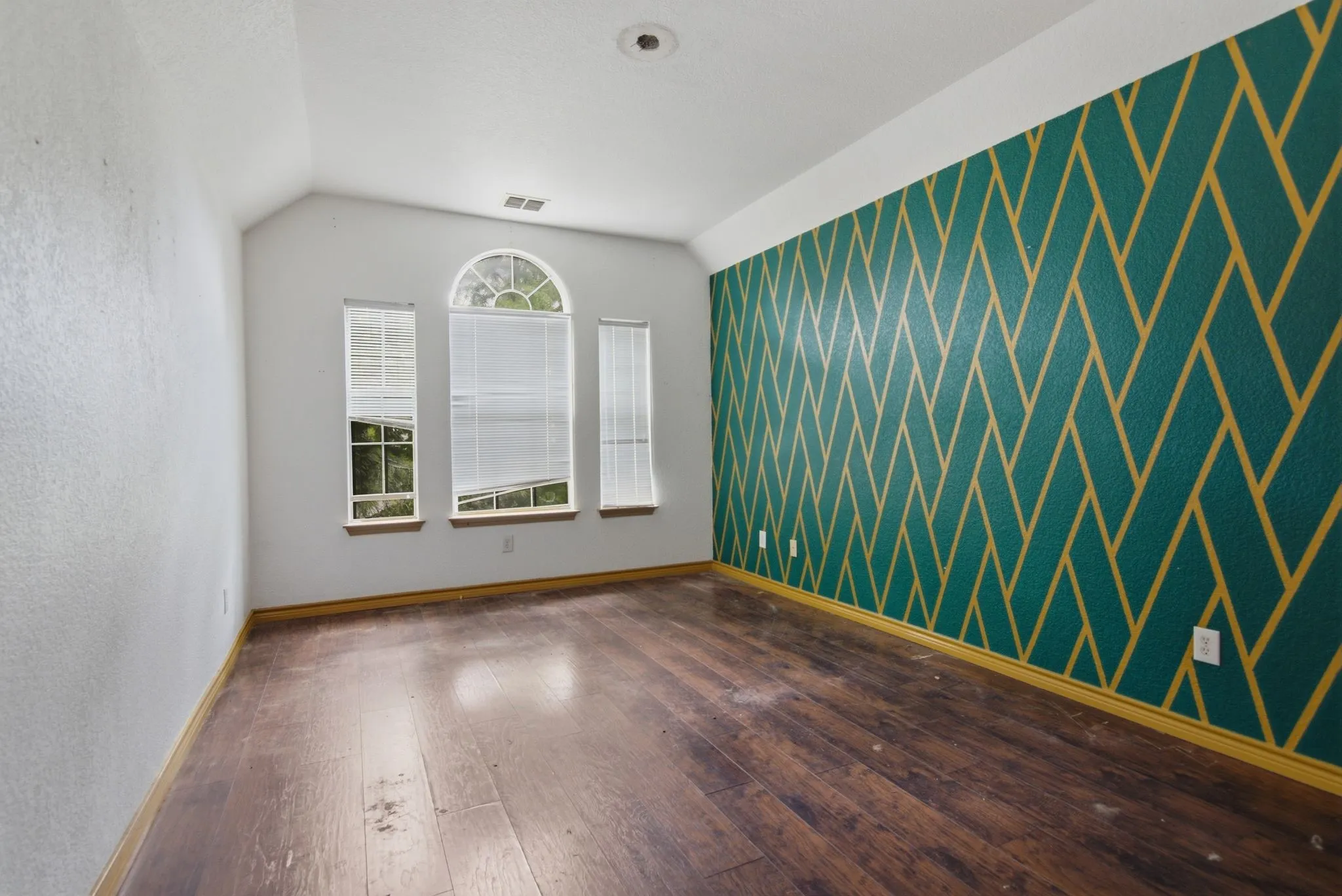 Spacious room featuring wood-finish flooring and a distinctive accent wall with a geometric pattern