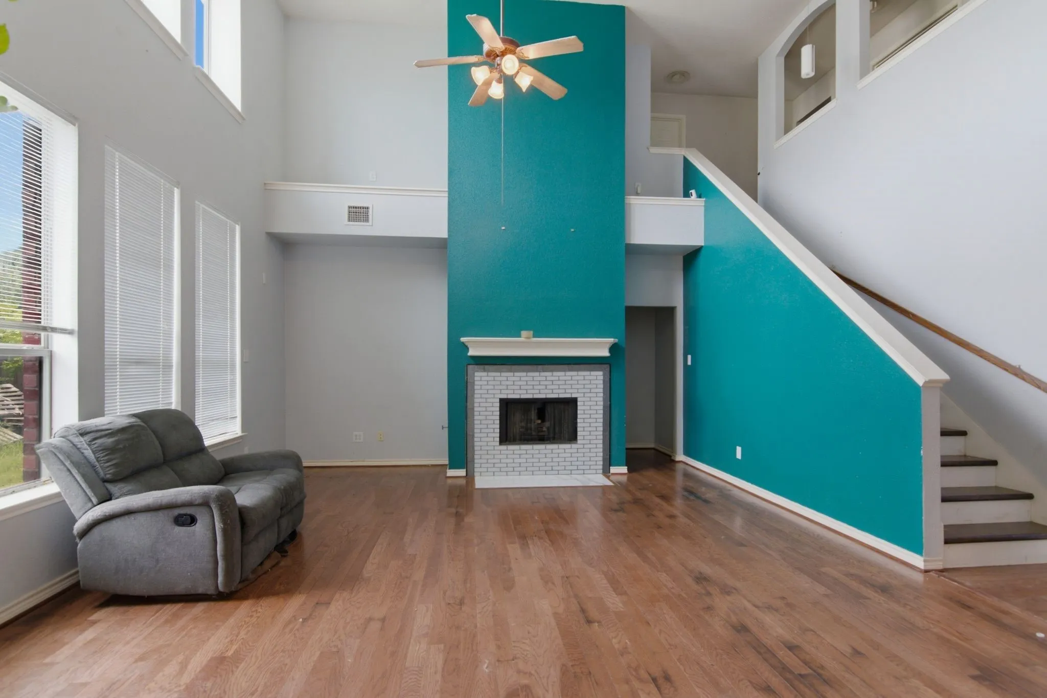 Living area with wood-finish flooring, a fireplace featuring a white brick surround and mantel, and a dual-height ceiling