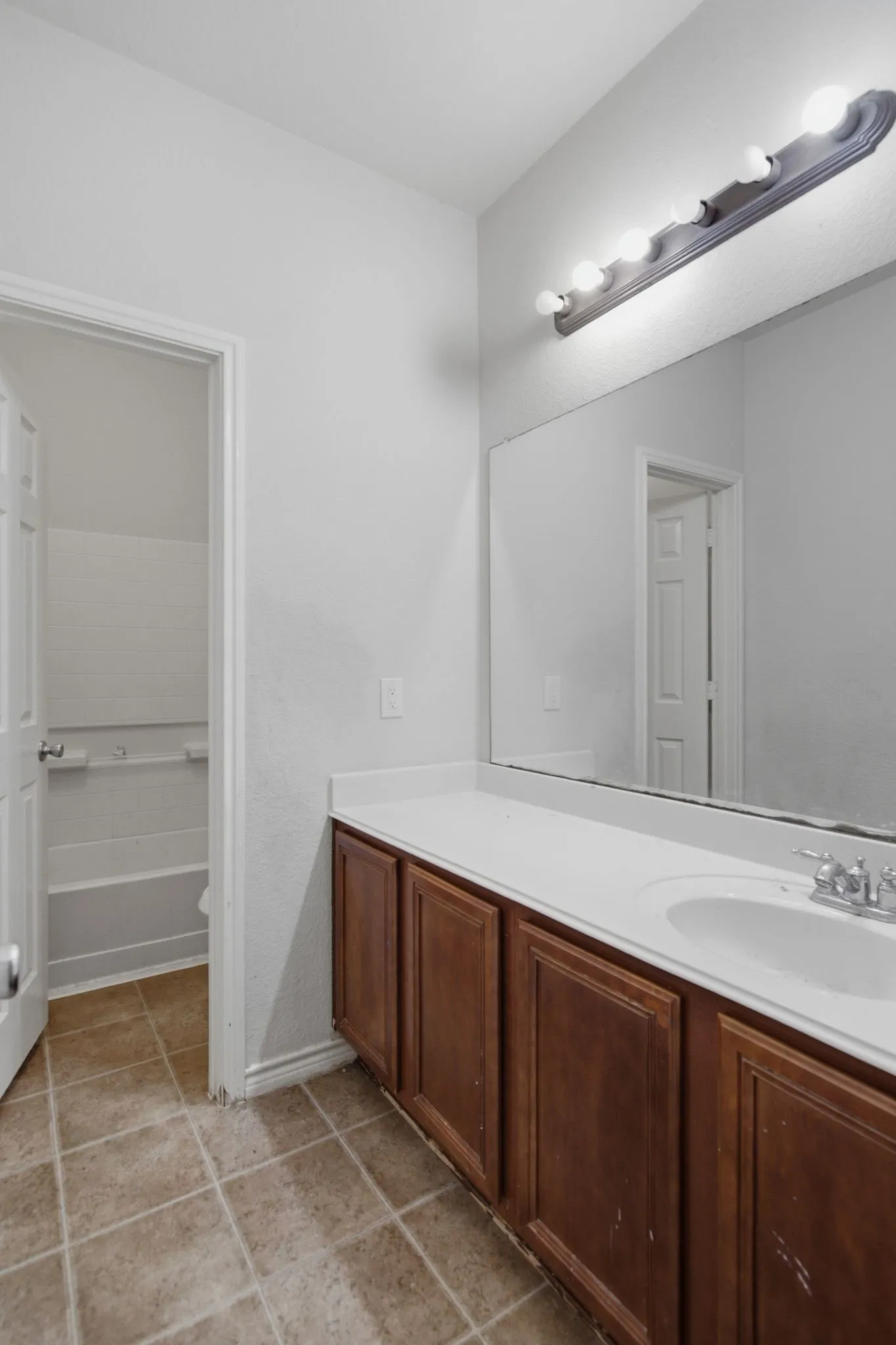 Bathroom vanity featuring a white countertop with an integrated sink, wood-finish cabinetry, and a full-width mirror